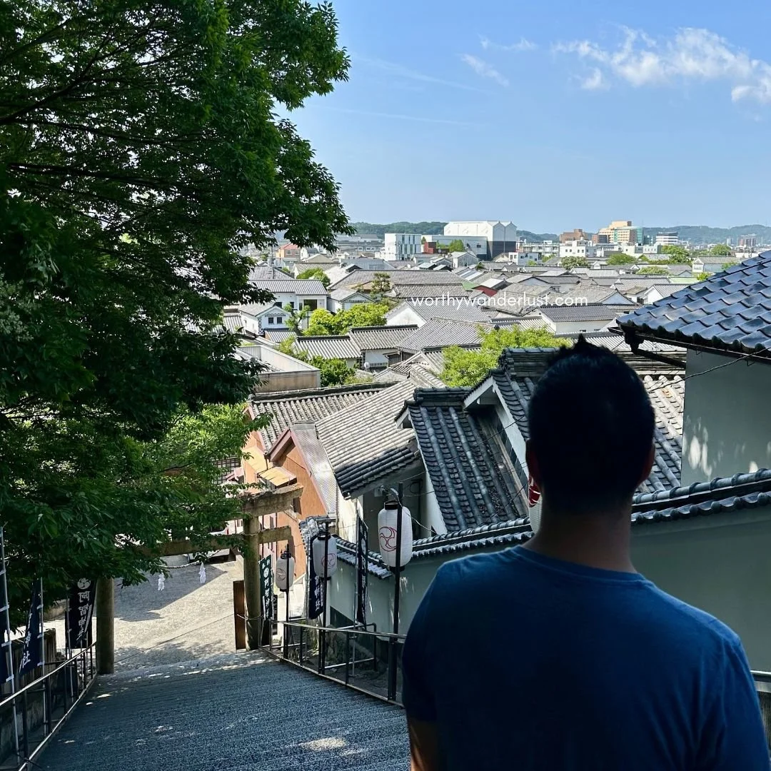 A man looking down at stairs leading up to Achi shrine, with views of the Bikan Historical Area