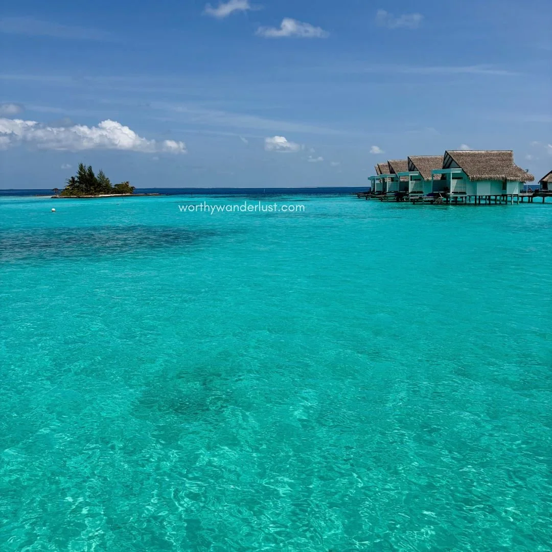 Turquoise ocean water with overwater villas and a small island at the back.