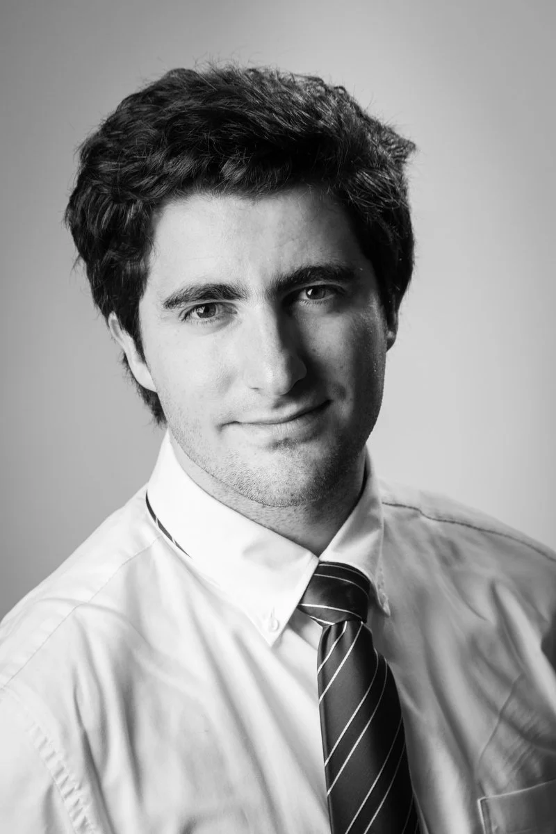 Portrait en noir et blanc d'un homme en chemise blanche et cravate rayée, souriant doucement.