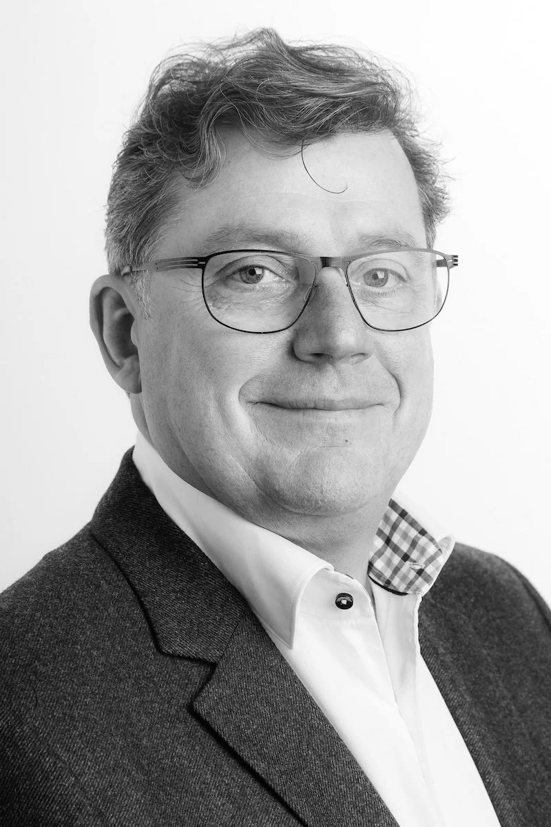 Portrait en noir et blanc d'un homme d'âge moyen portant des lunettes et une veste de costume.