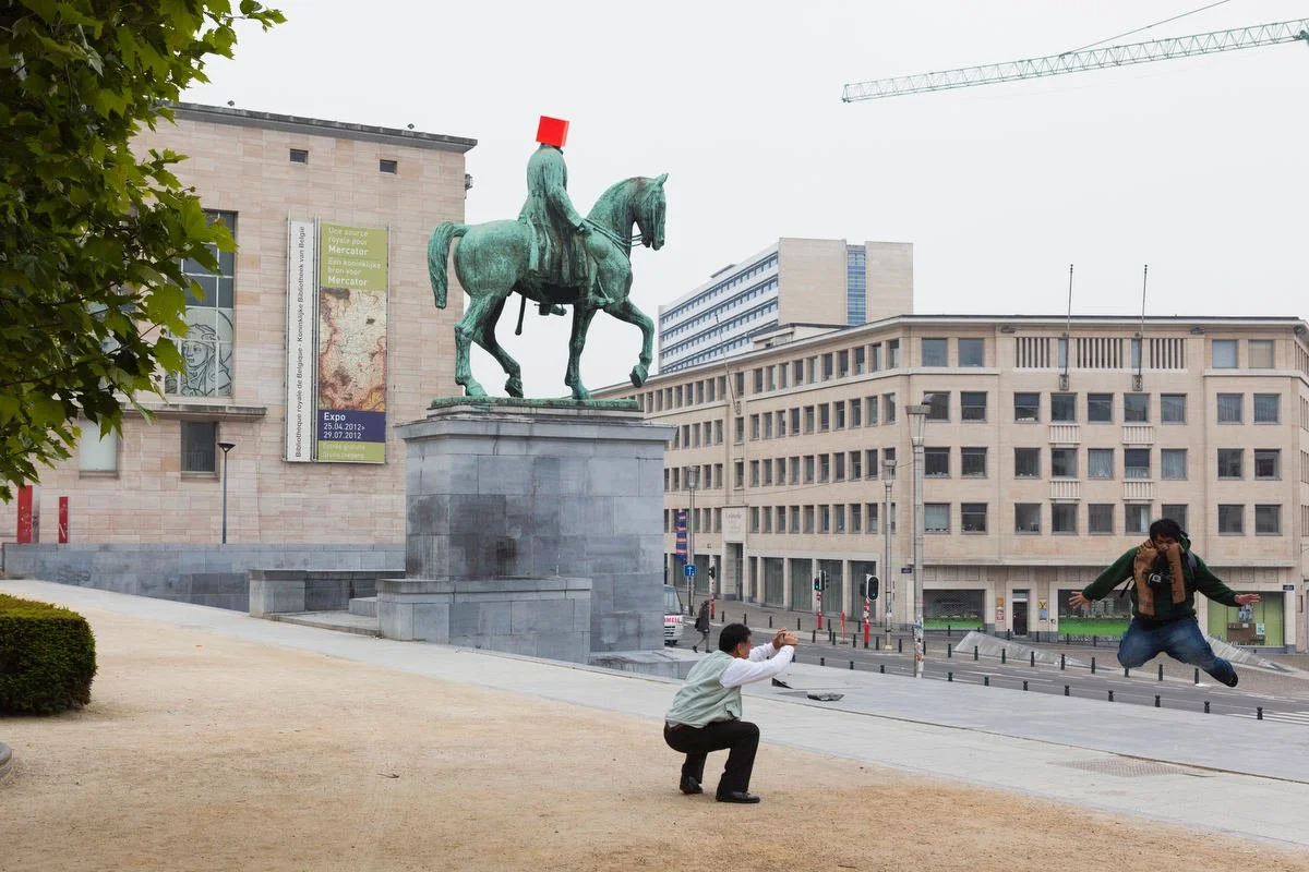 Person jumping in front of equestrian statue in urban setting.