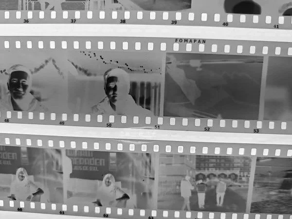 Black and white film strip with images of two men and a group of children in an outdoor setting.