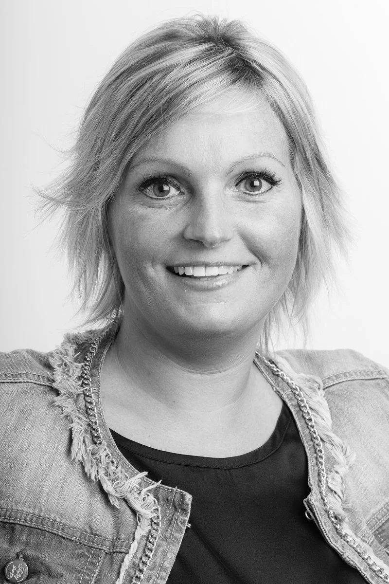 Portrait en noir et blanc d'une femme souriante aux cheveux courts portant une veste en jean.