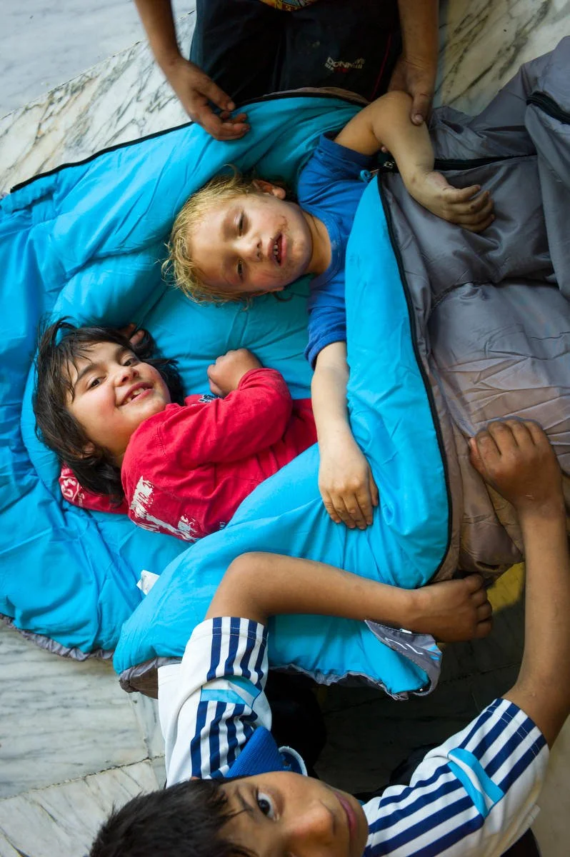 Children lying in sleeping bags on the ground, smiling and resting.