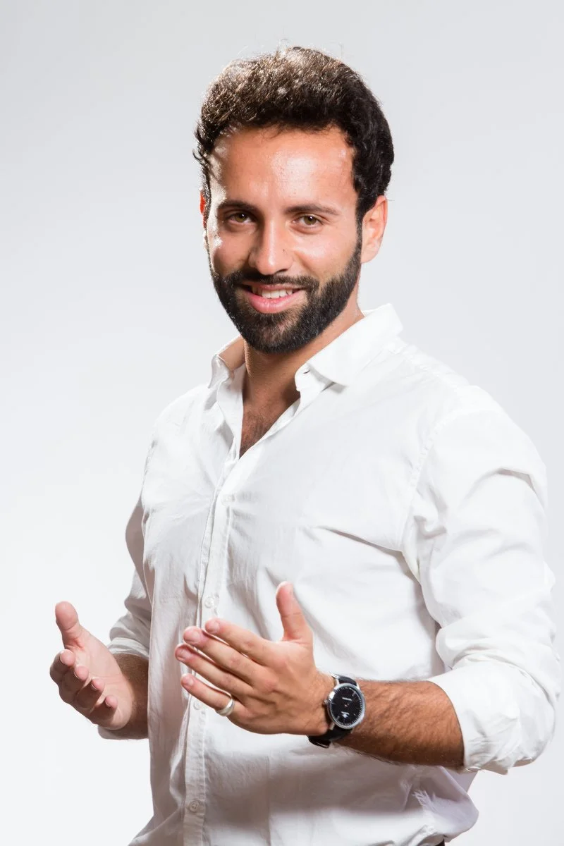 Homme souriant en chemise blanche avec une montre, faisant un geste des deux mains.