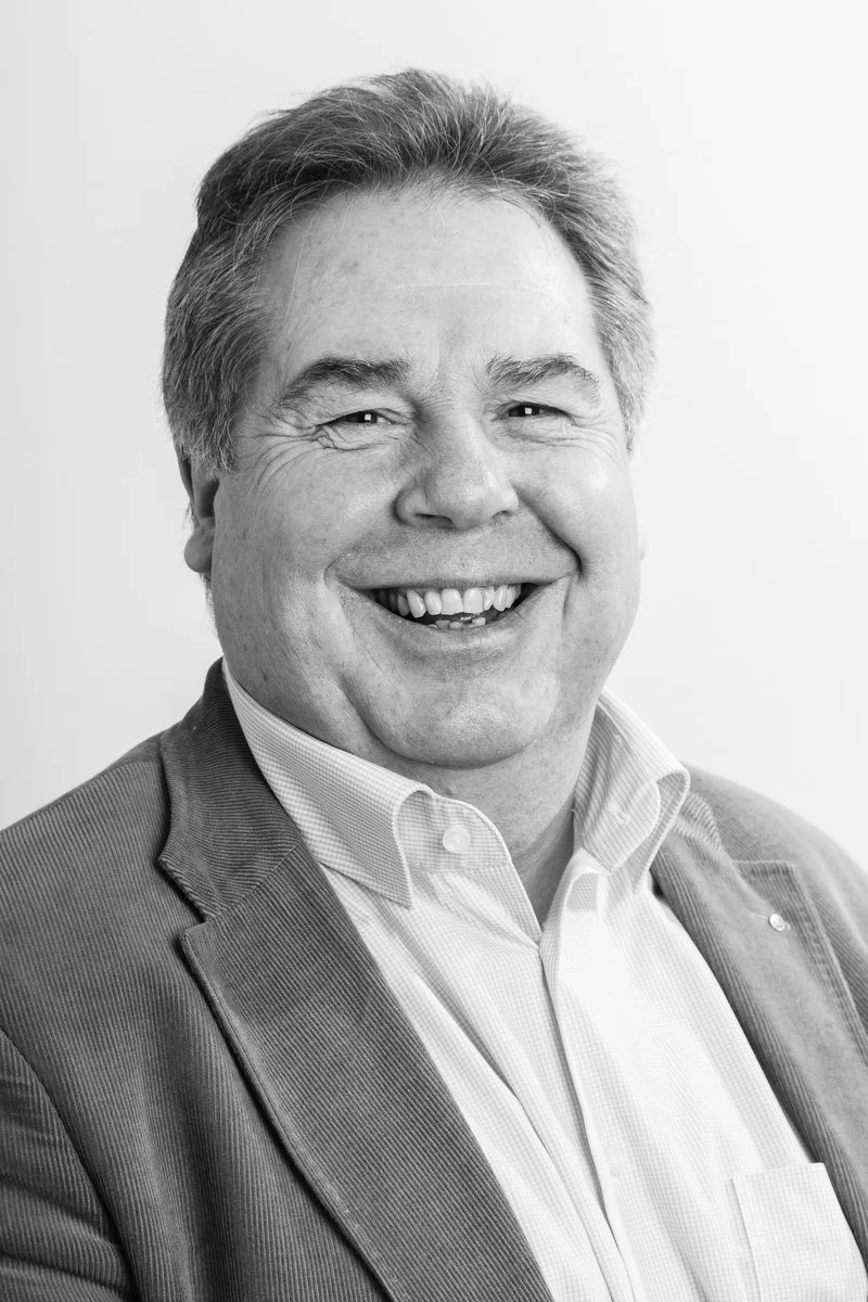 Homme souriant en blazer et chemise à col, portrait en noir et blanc.