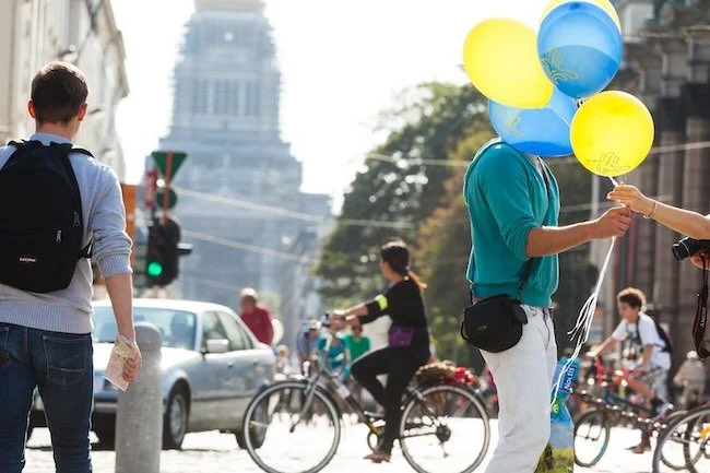 Man with blue and yellow balloons covering his face in the center of Brussels