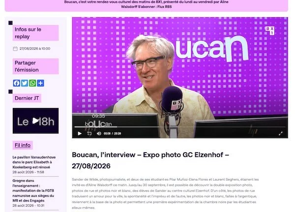 A man with glasses and gray hair is smiling while speaking into a microphone during an interview on a video streaming platform. The background features a purple screen with white dots and the word 'Ucan'.
