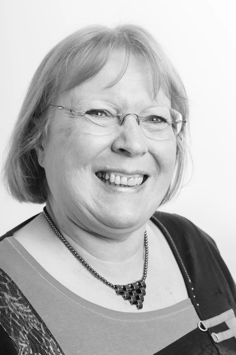 Photo en noir et blanc d'une personne souriante portant des lunettes et un collier.