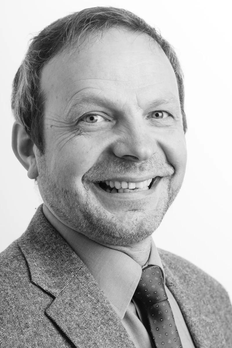 Portrait en noir et blanc d'un homme souriant en costume-cravate.