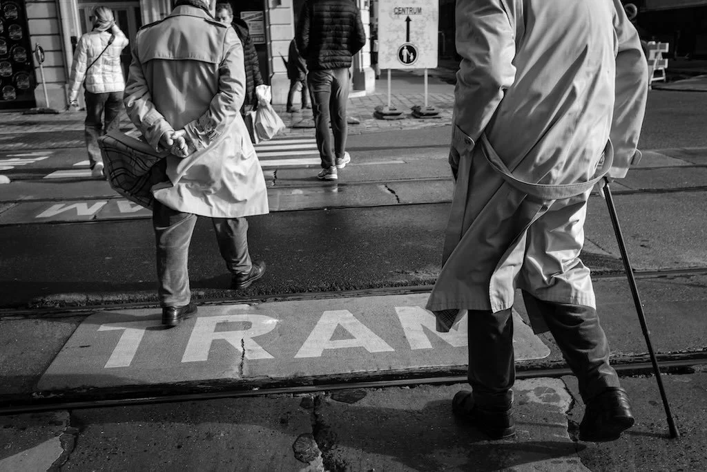 Black and white street photo of two elderly men crossing a road in the wind near tram tracks in Antwerp