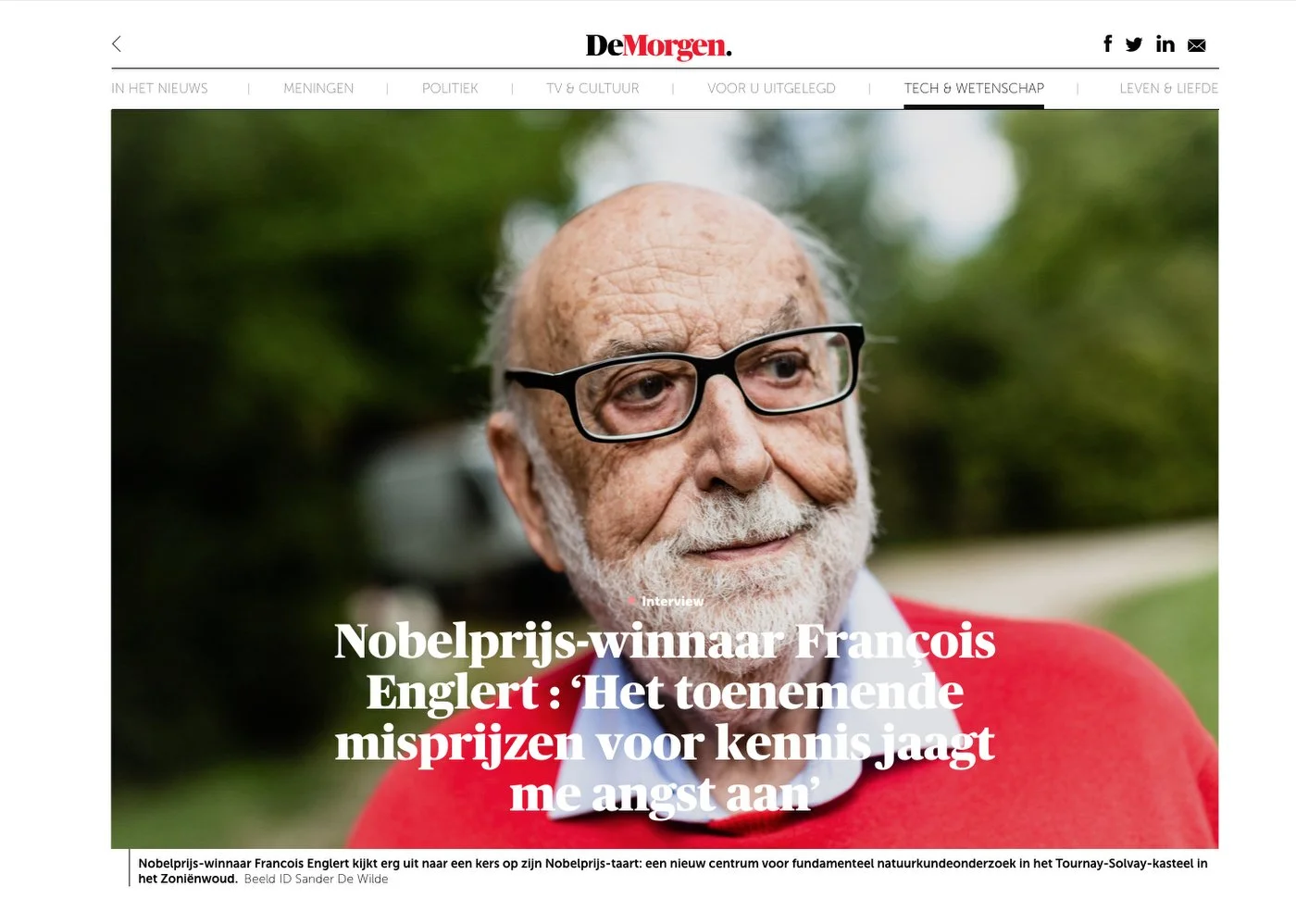 Homme âgé à lunettes vêtu d'un pull-over rouge sur un fond flou en extérieur, avec en surimpression le texte néerlandais "Nobelprijs-winnaar Francois Englert..." sur le site De Morgen.