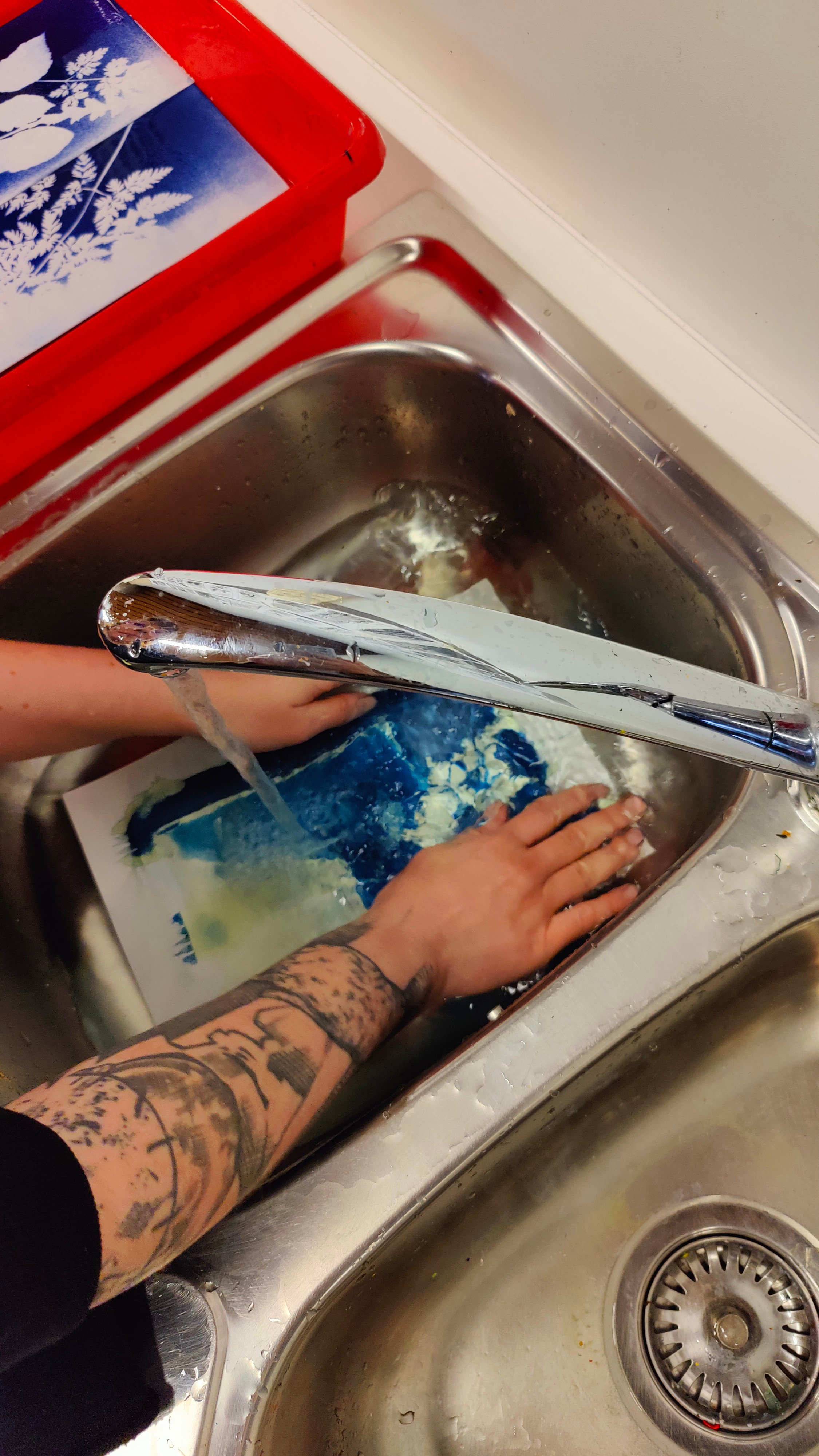 Photo of a girl with tattoos washing a cyanotype print with water