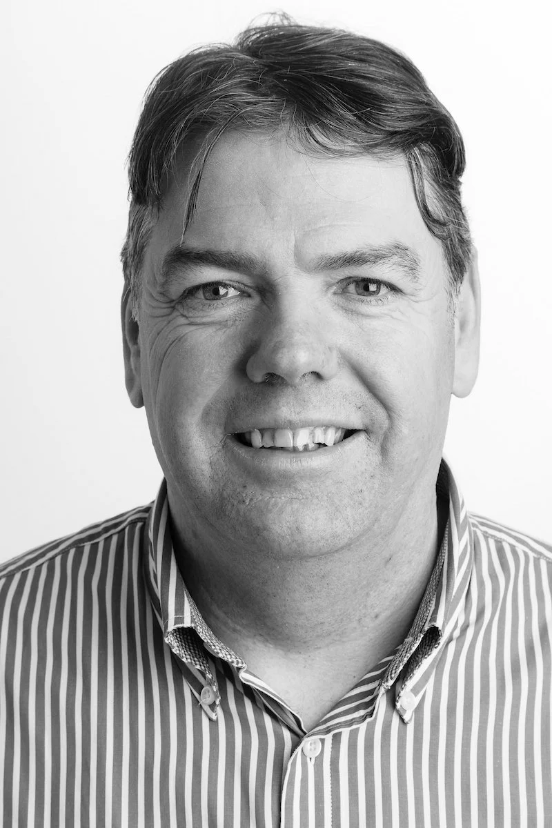 Portrait en noir et blanc d'un homme souriant portant une chemise rayée.