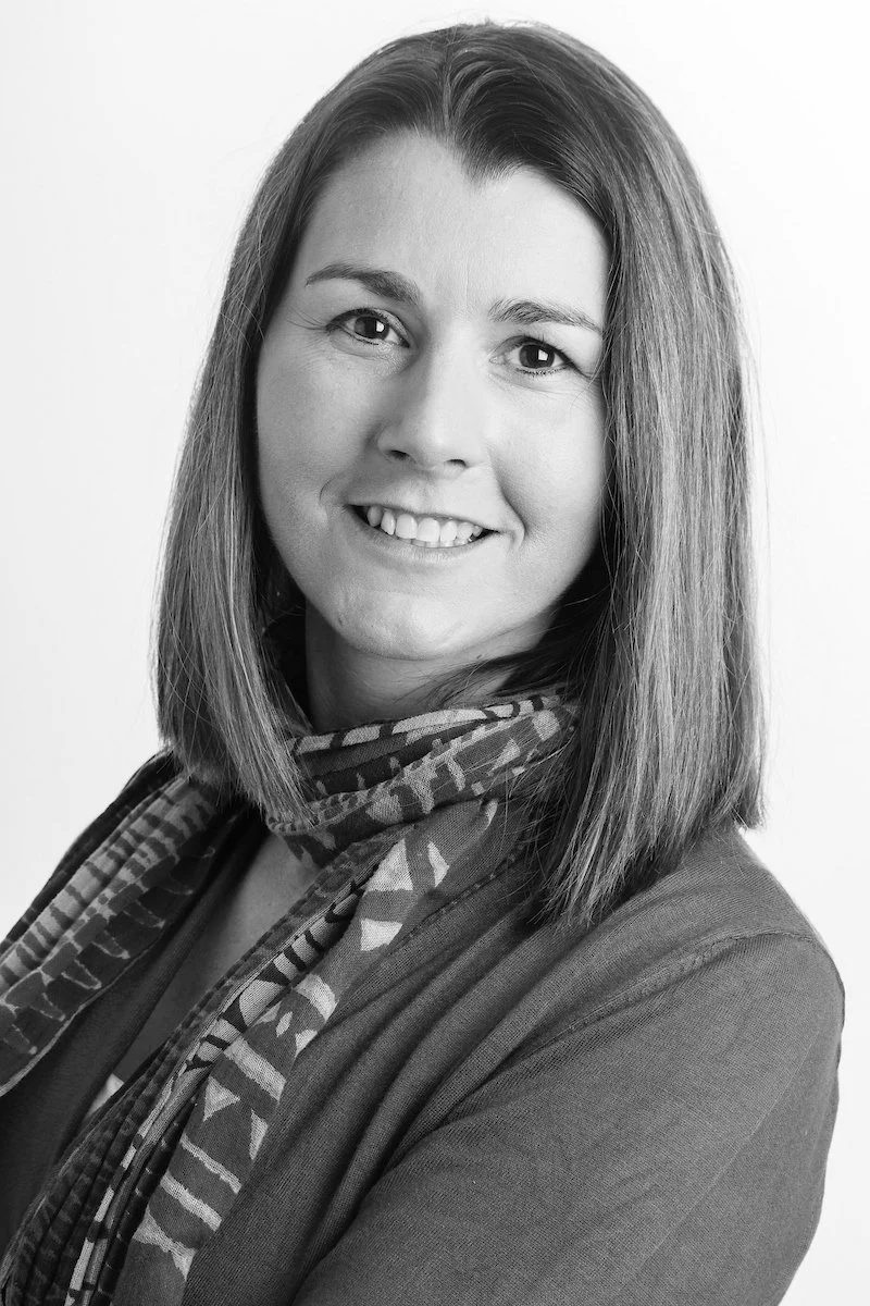 Portrait en noir et blanc d'une femme souriante aux cheveux mi-longs portant un foulard à motifs et un haut de couleur claire.