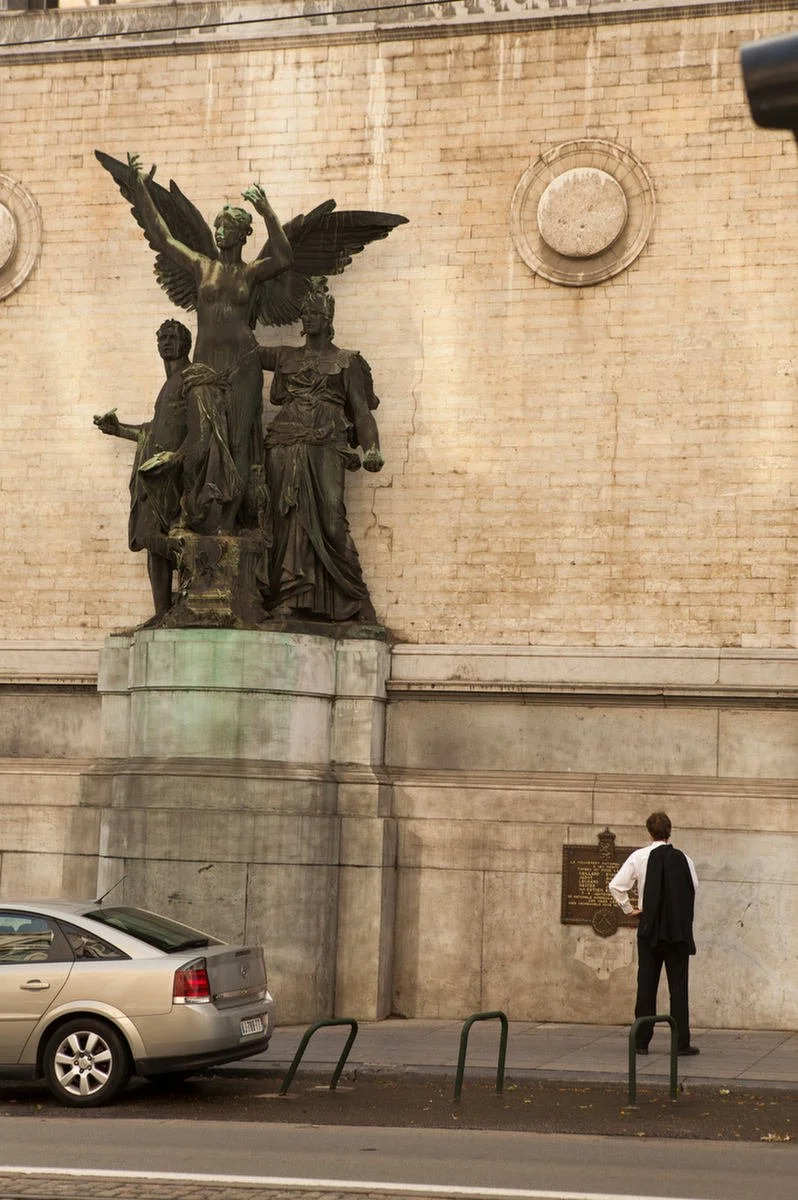 A person standing near a historic statue on a street.