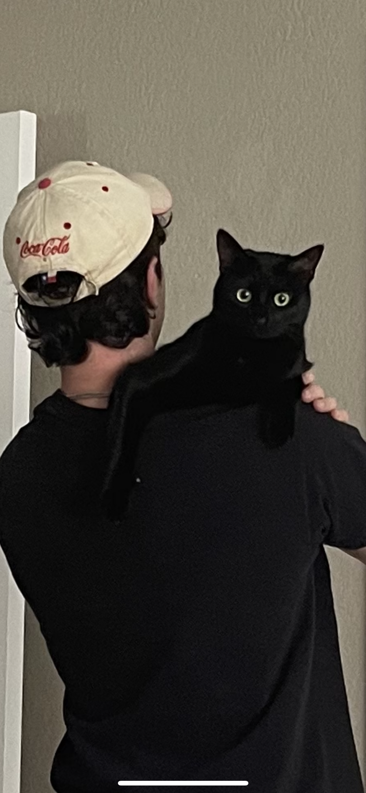 Kamran, seen from behind in a cap, holding his black cat, Marnie, on his shoulder.