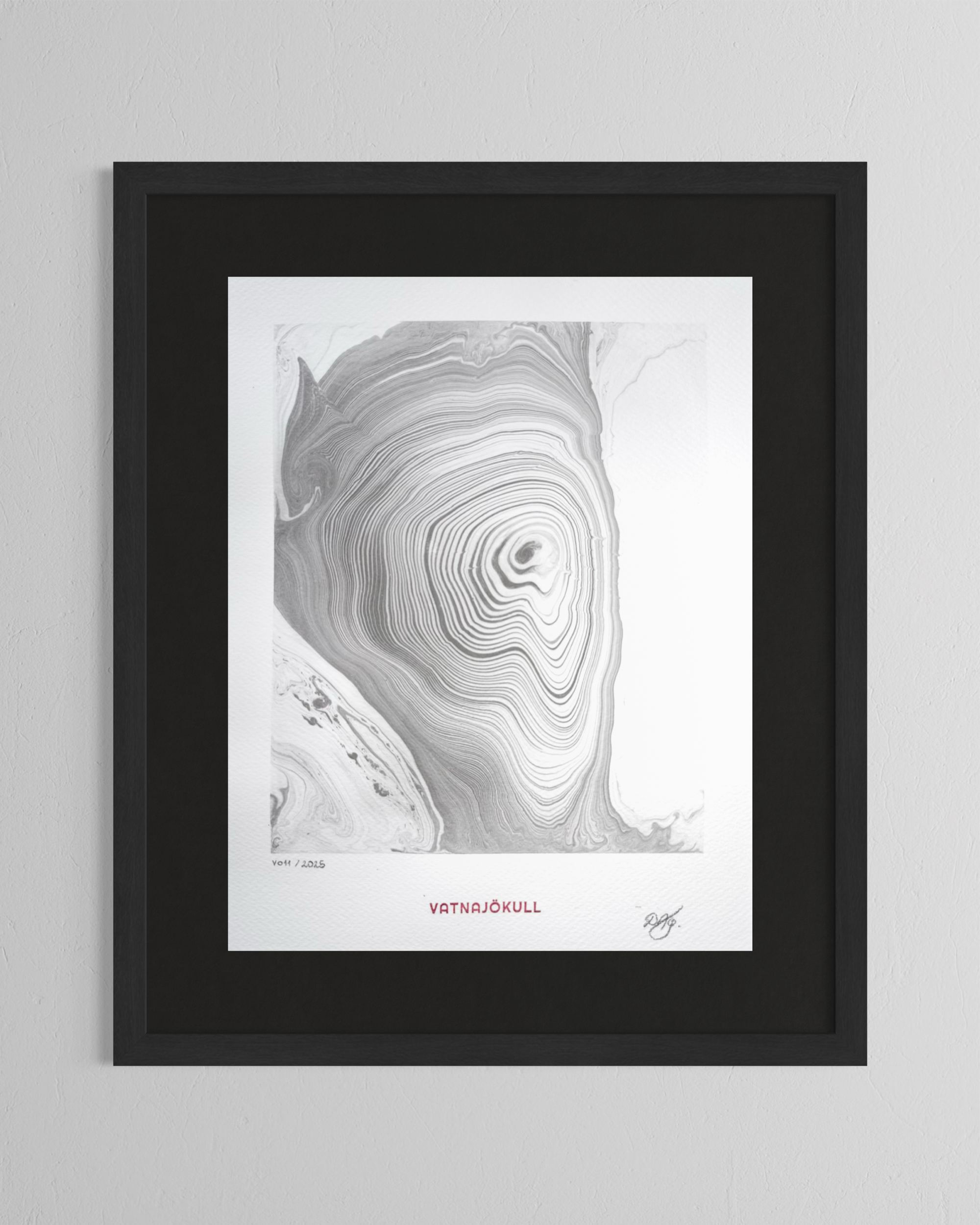 Black and white abstract art with concentric swirling lines resembling a topographical map or wood grain, framed on a white wall. The artwork has the title "Vatnajökull" in red and a signature at the bottom right.