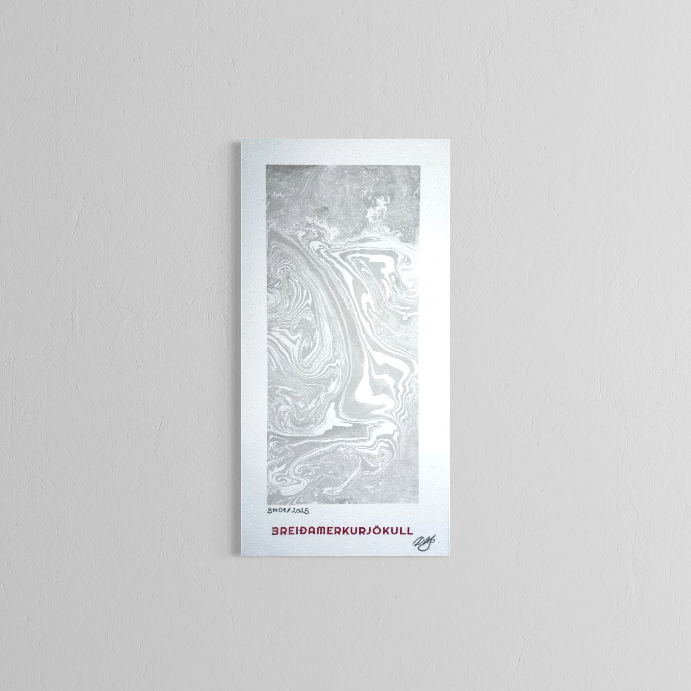 A handmade print featuring a grayscale marbled abstract profile of a face with text in Icelandic, including "BREIDDAMERKURJÖKULL," on a white wall.