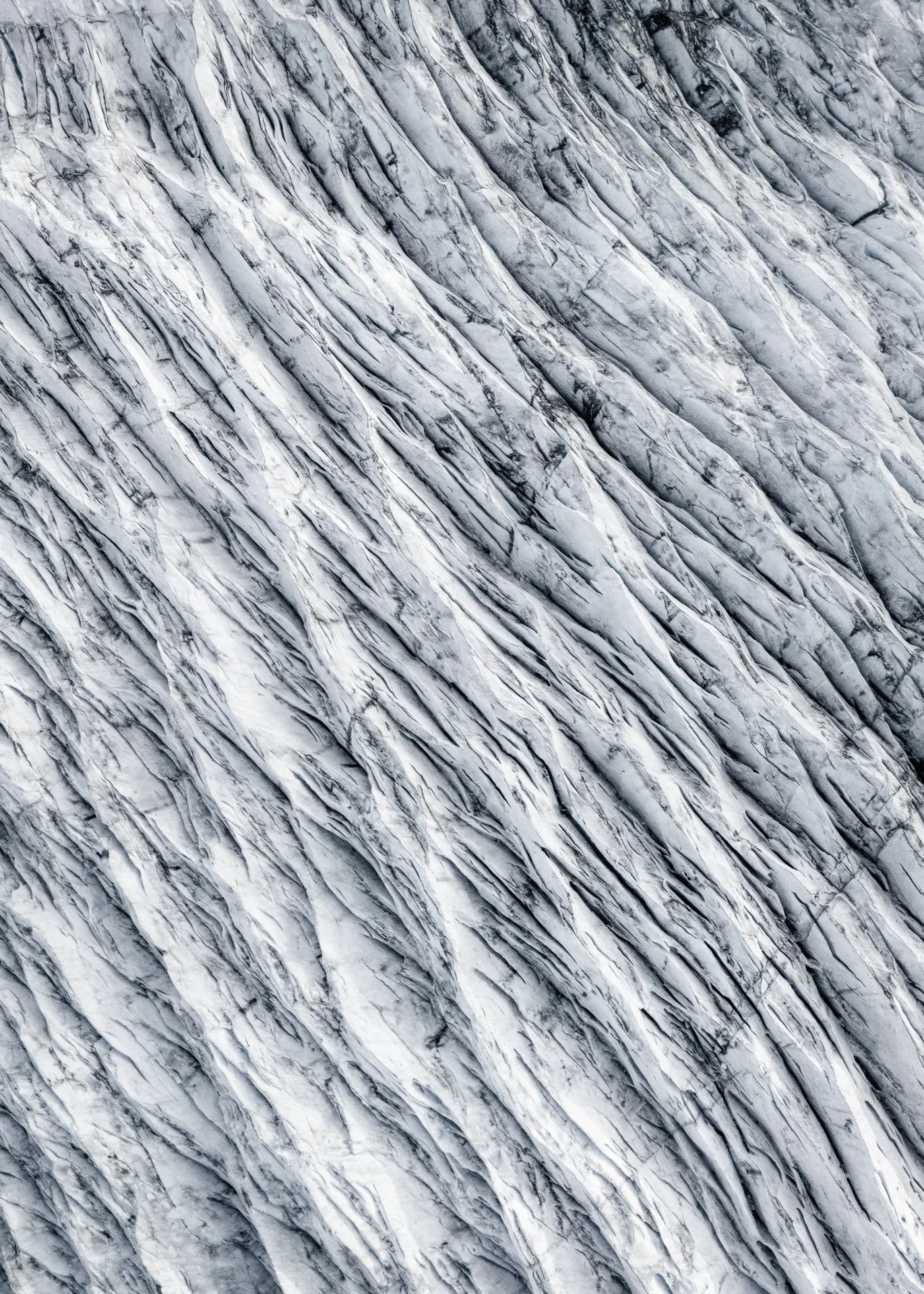 Close-up view of a wall or natural formation with diagonal layered white and gray marble or stone with black veining.