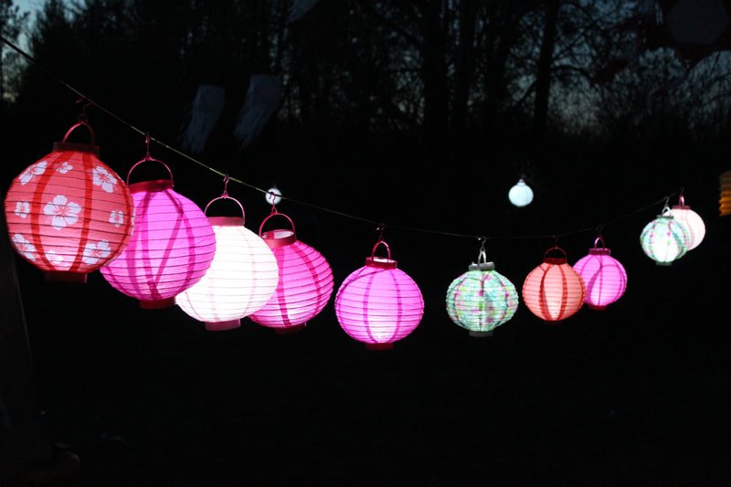 Colorful paper lanterns hanging in a row, illuminated at night against a dark background.