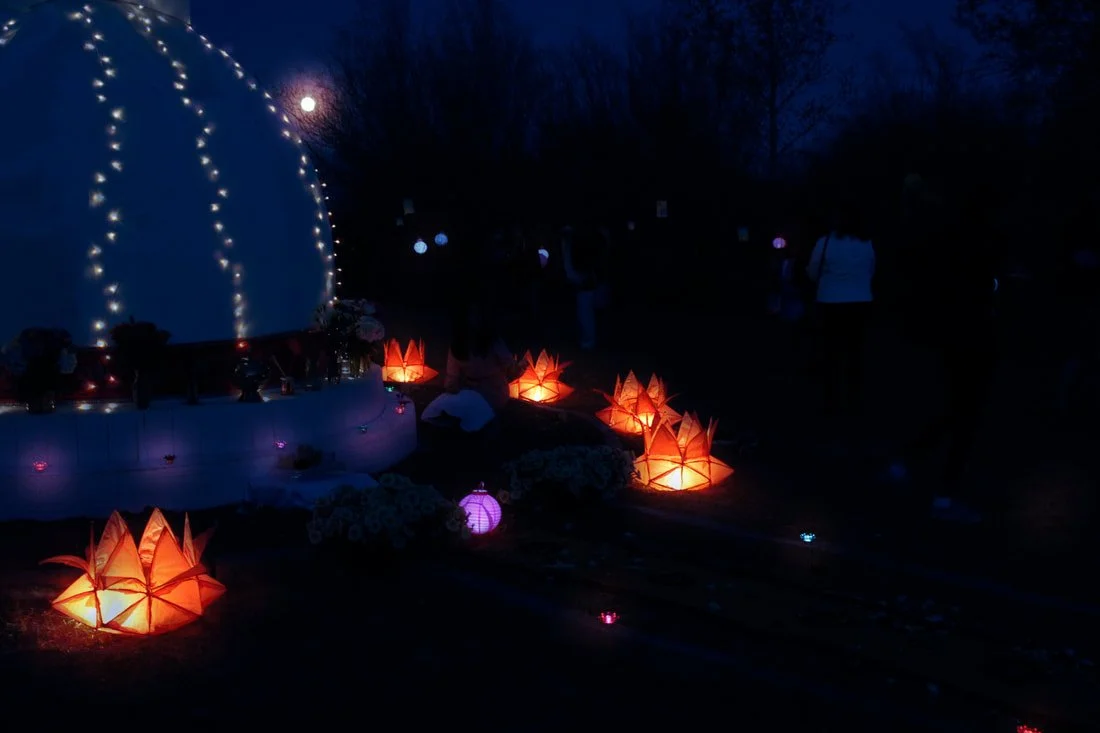 Decorative outdoor scene at night with illuminated star-shaped lanterns, string lights on a dome, and people in the background.
