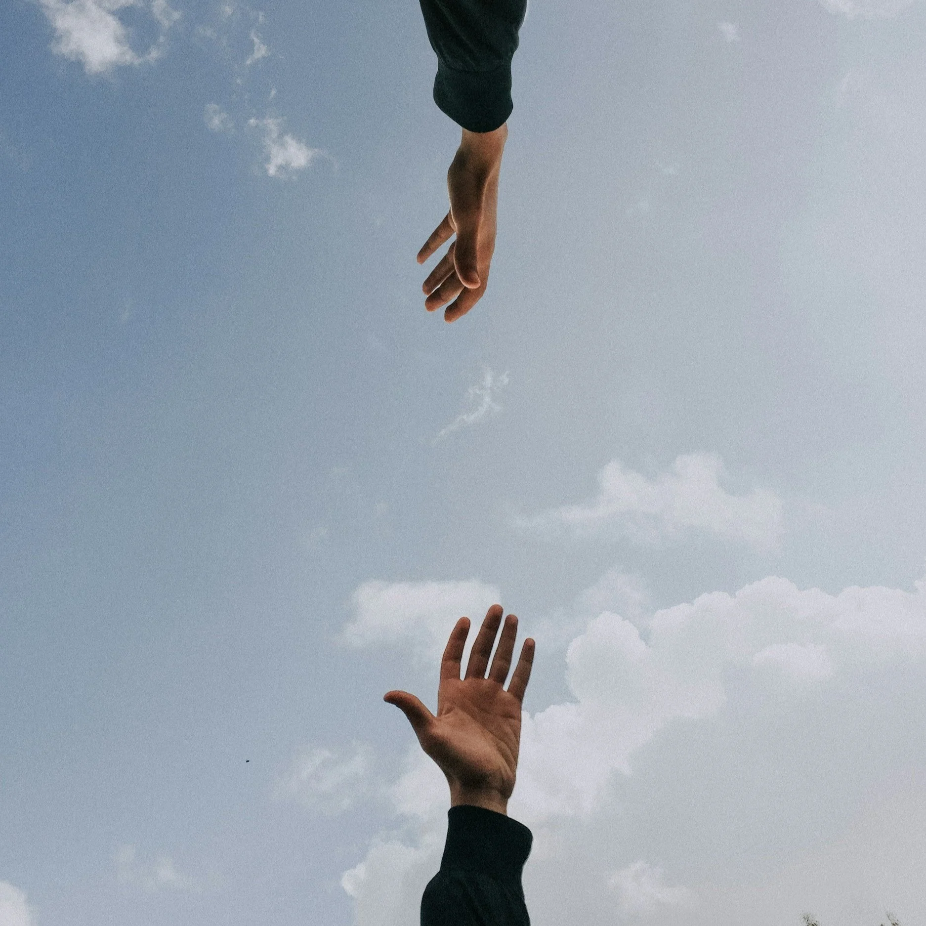 Two hands reaching towards each other against a cloudy blue sky.