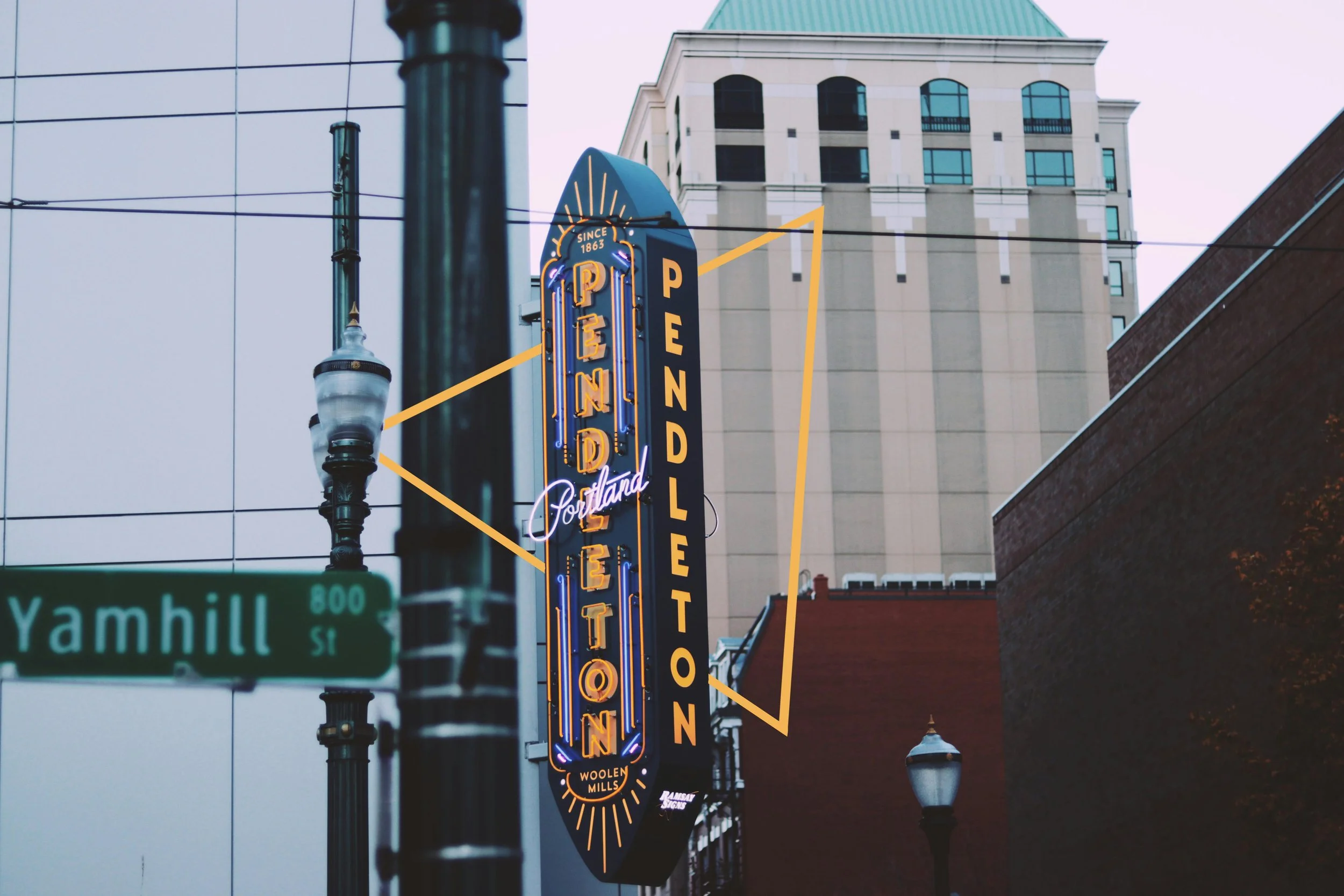 Vertical neon sign for Portland open on a downtown street, with a street lamp and Yamhill street sign in foreground, and tall buildings in background.