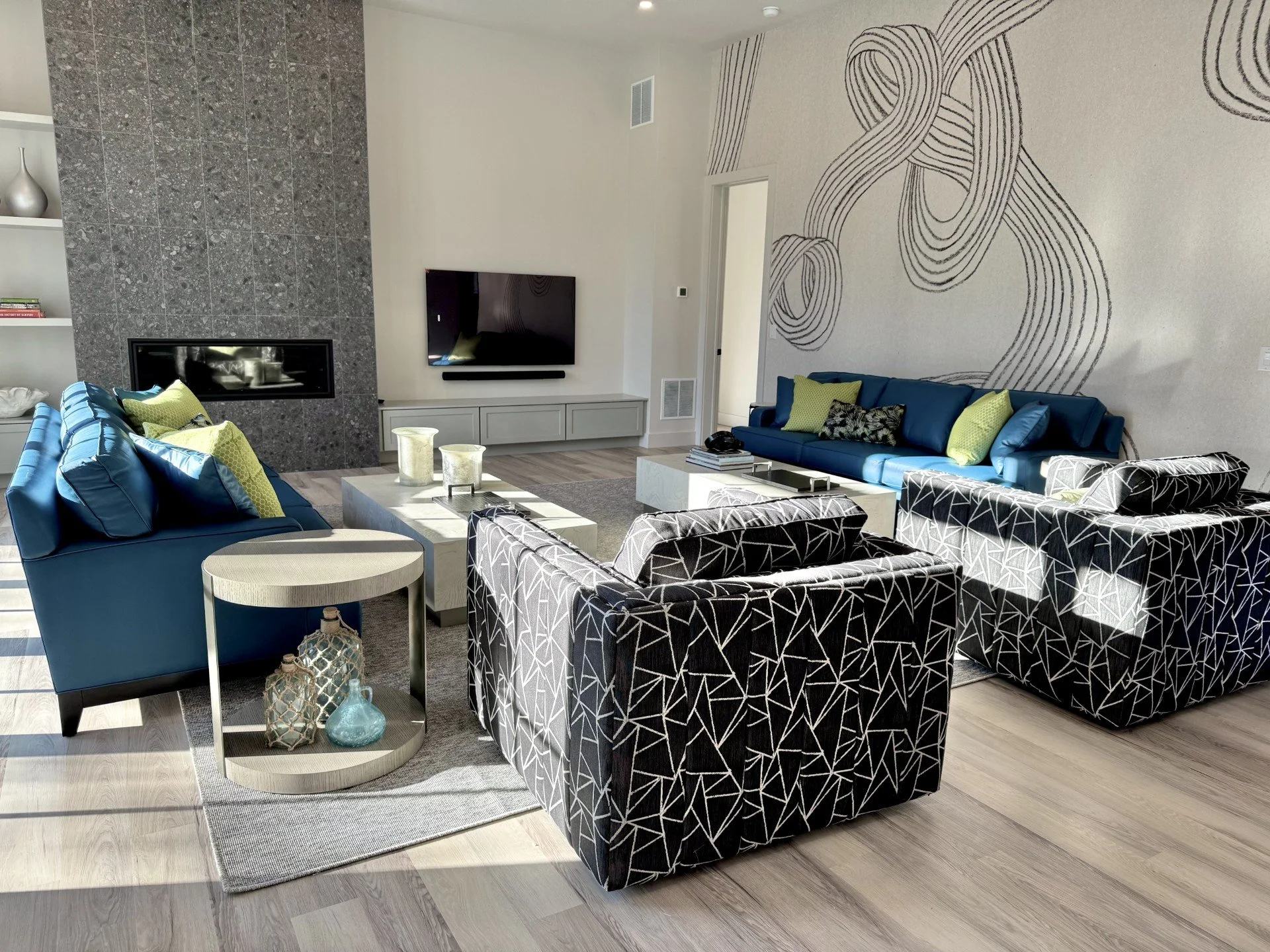 Modern beach house living room with bold scribble wallpaper, teal faux leather sofas, swivel chairs, and dark fireplace built-ins