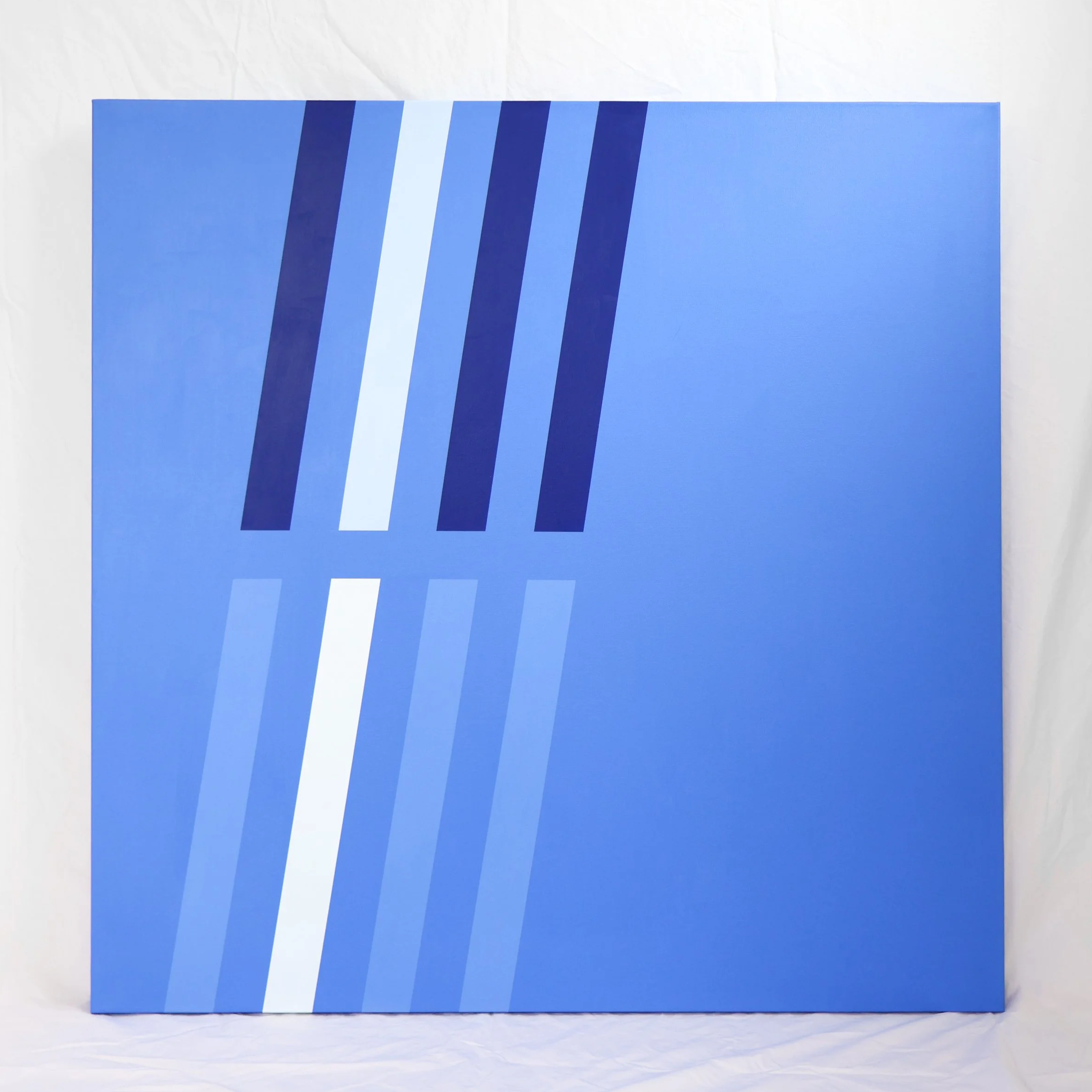 A blue square canvas painting with dark blue and light blue diagonal stripes towards the right side.