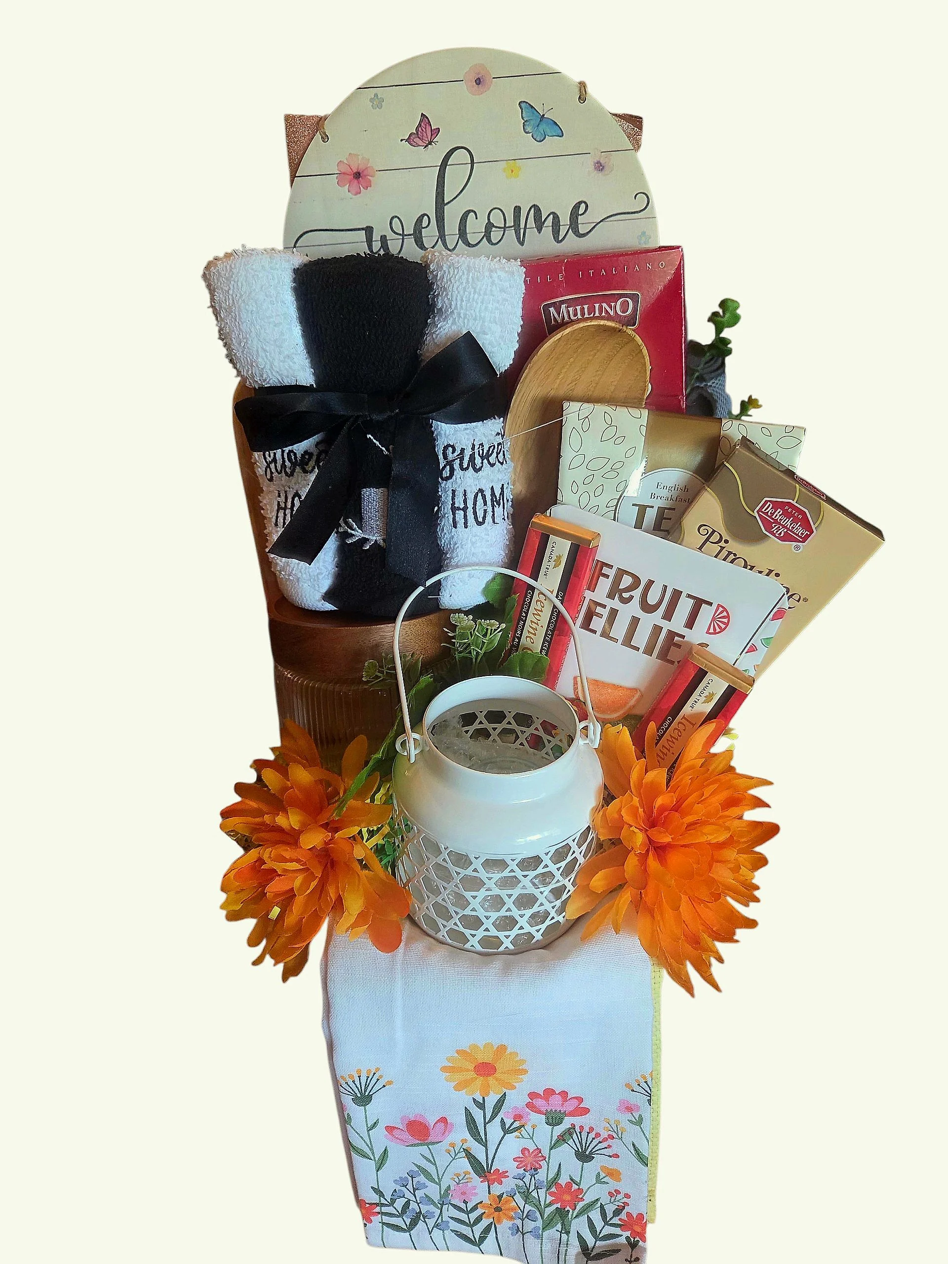 A decorative gift basket with a floral theme, including a welcome sign, a pair of striped socks, chocolate, seeds, a watering can, and orange artificial flowers.