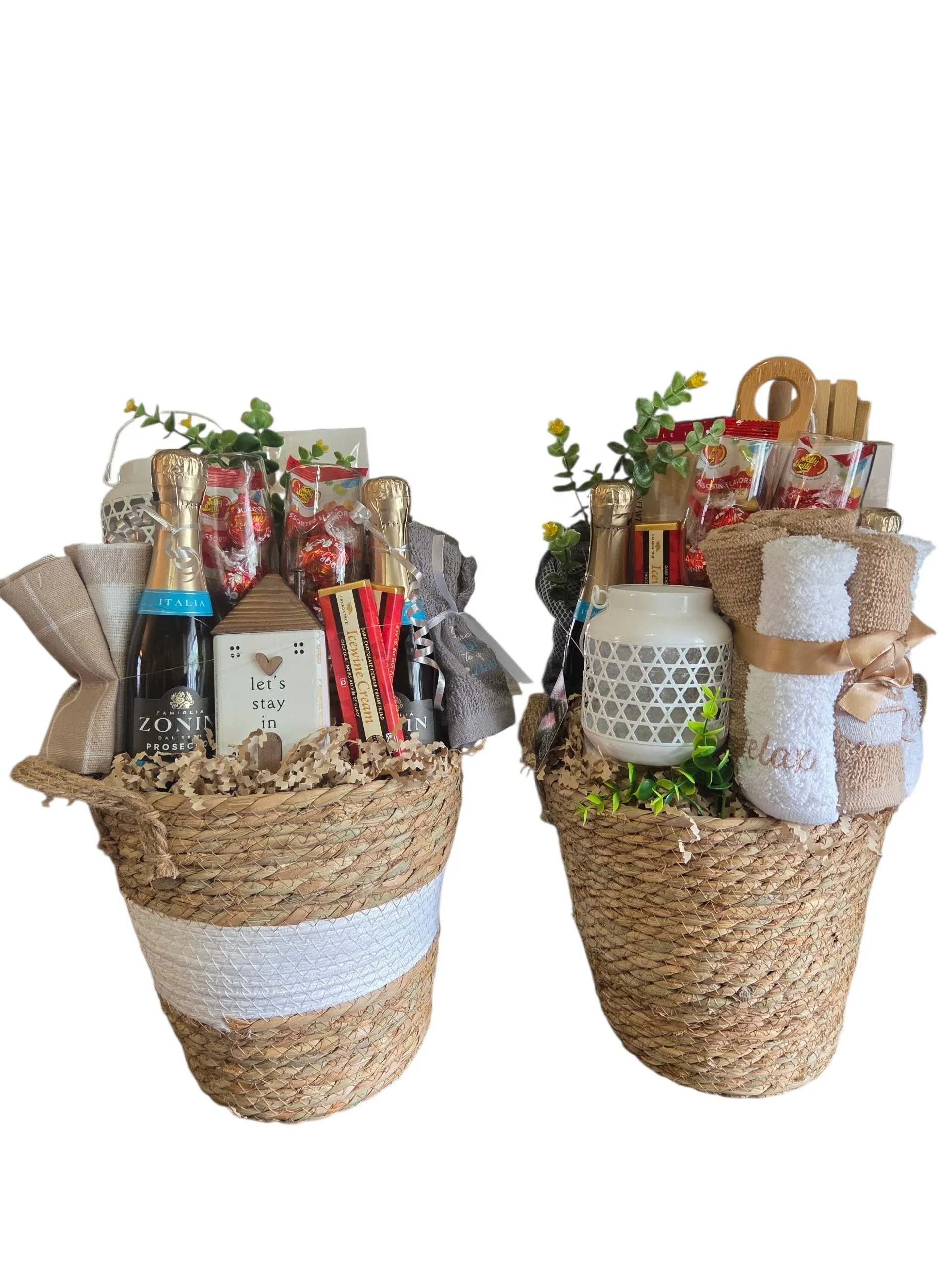 Two decorative woven baskets filled with various gift baskets, bottles, and rolled towels, decorated with greenery and ribbons.