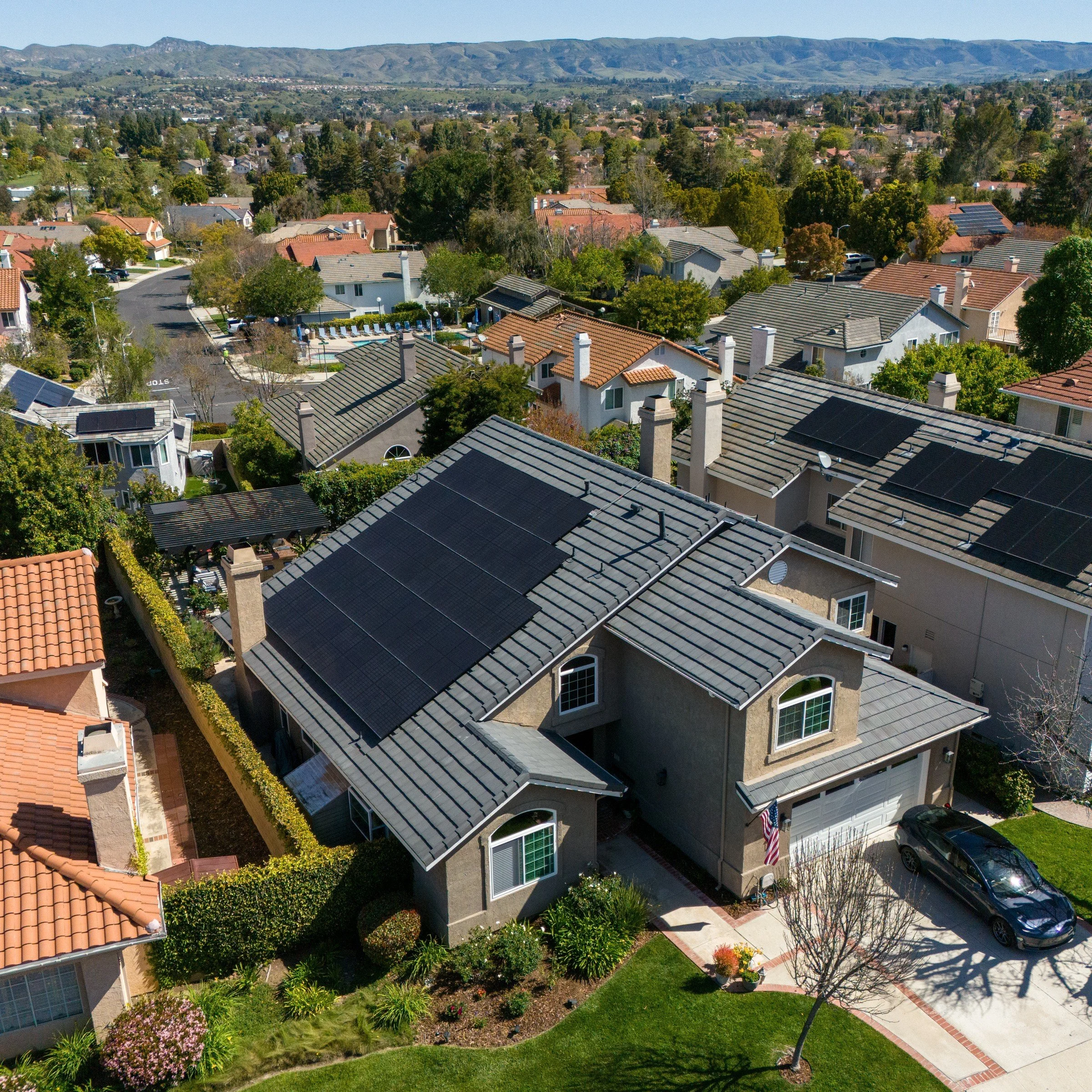 Aerial of a Moorpark two-story home with a dark gray tile roof, rooftop solar, and rolling hills beyond the street