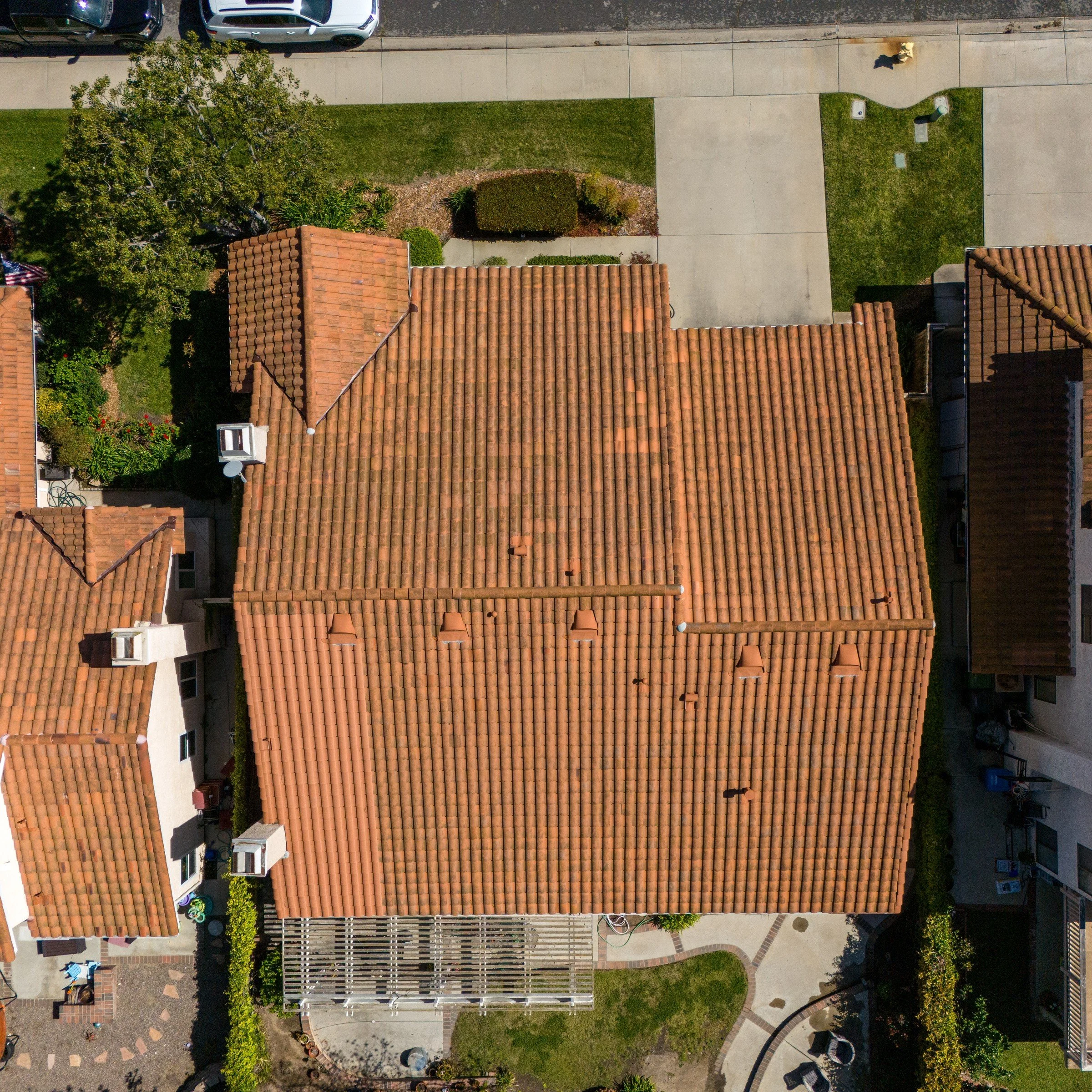Aerial of a Moorpark home with a terracotta tile roof, backyard patio cover, and neighboring tile roofs from directly above