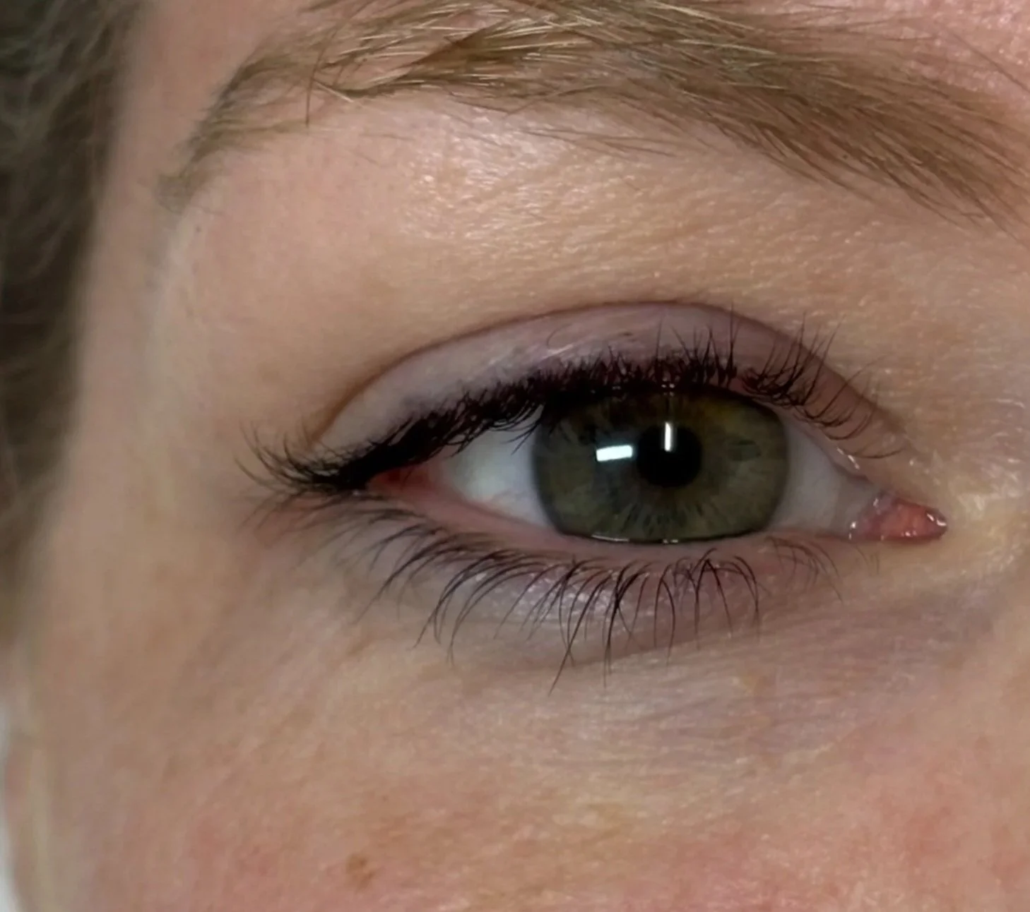 Close-up of a person's eye with makeup, including eyeliner and mascara, showing the iris and eyelashes.