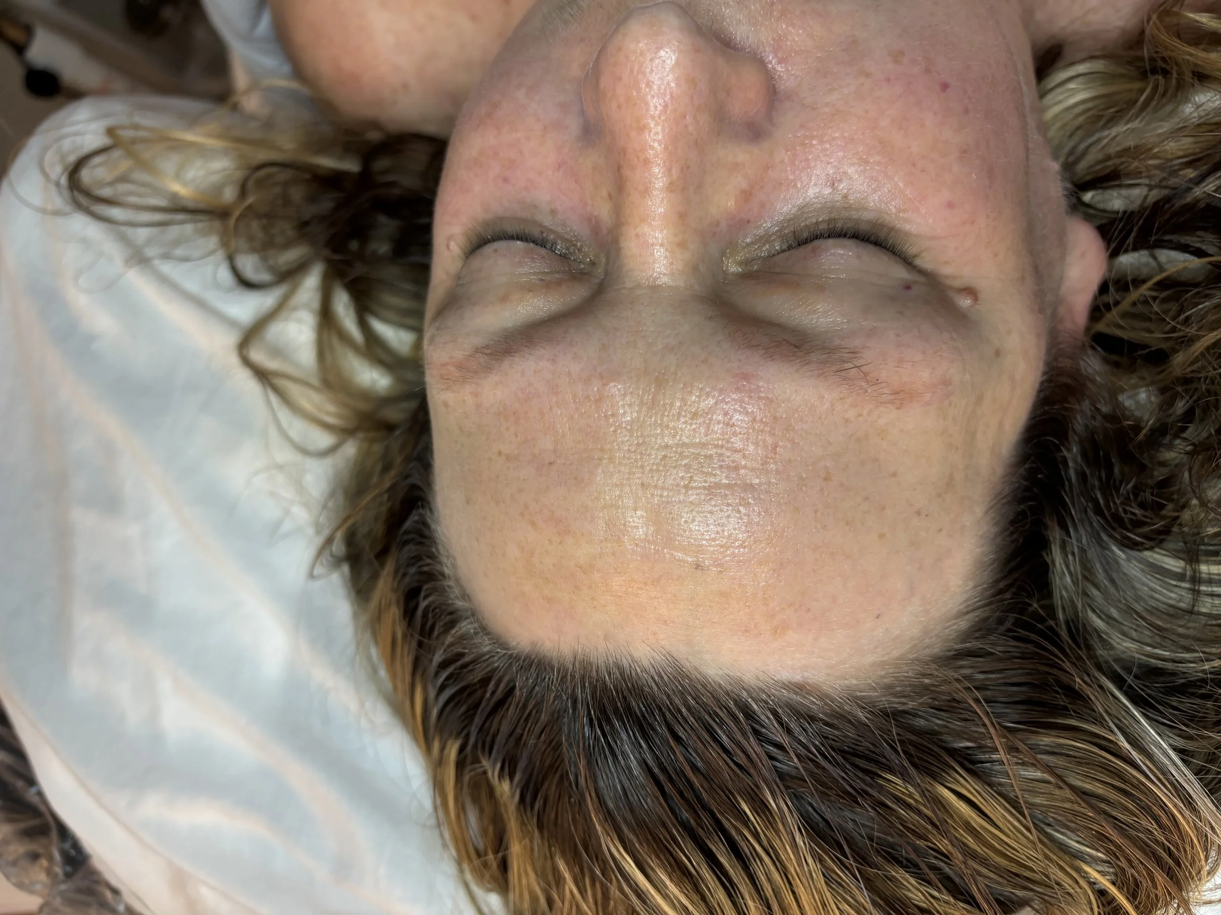 Close-up of a person with closed eyes lying down, showing skin with freckles and makeup, and hair spread around the head.