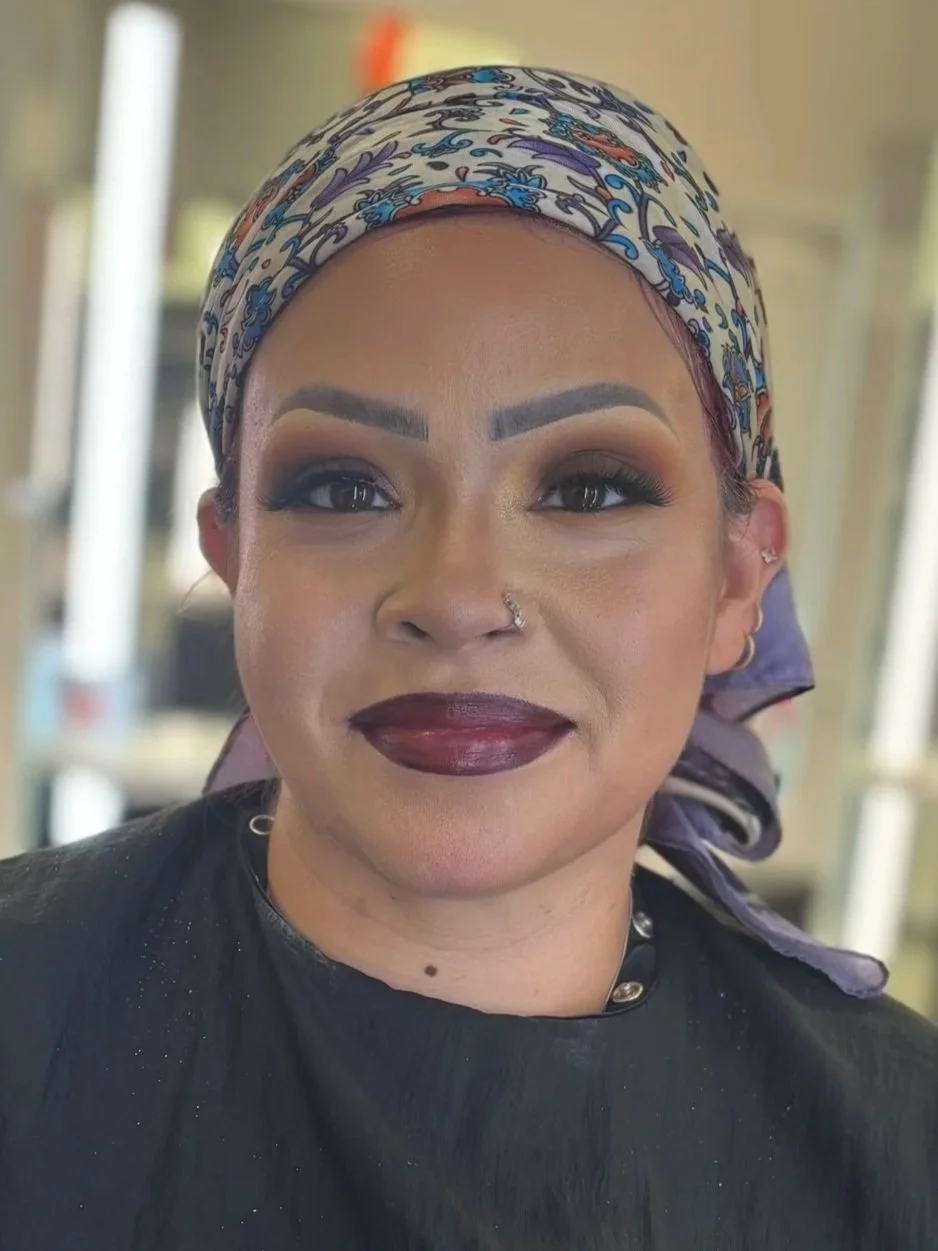 A woman with dark makeup and a colorful headscarf smiling at the camera.