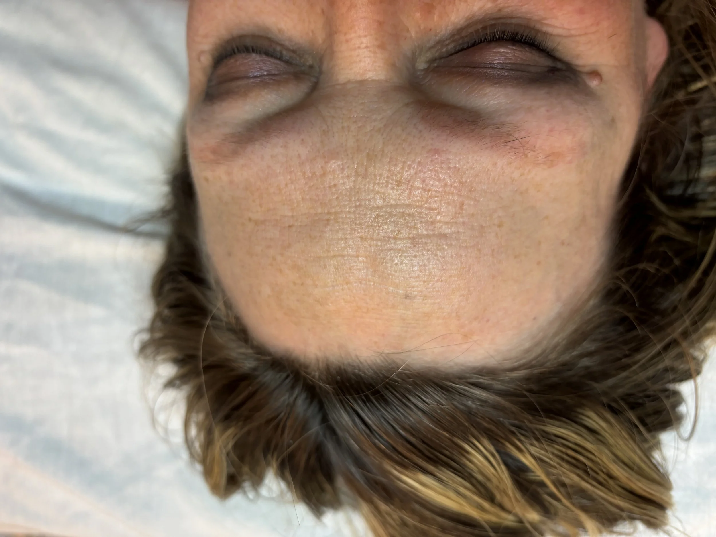 Close-up of a person lying down with closed eyes, showing skin texture and brown, wavy hair.