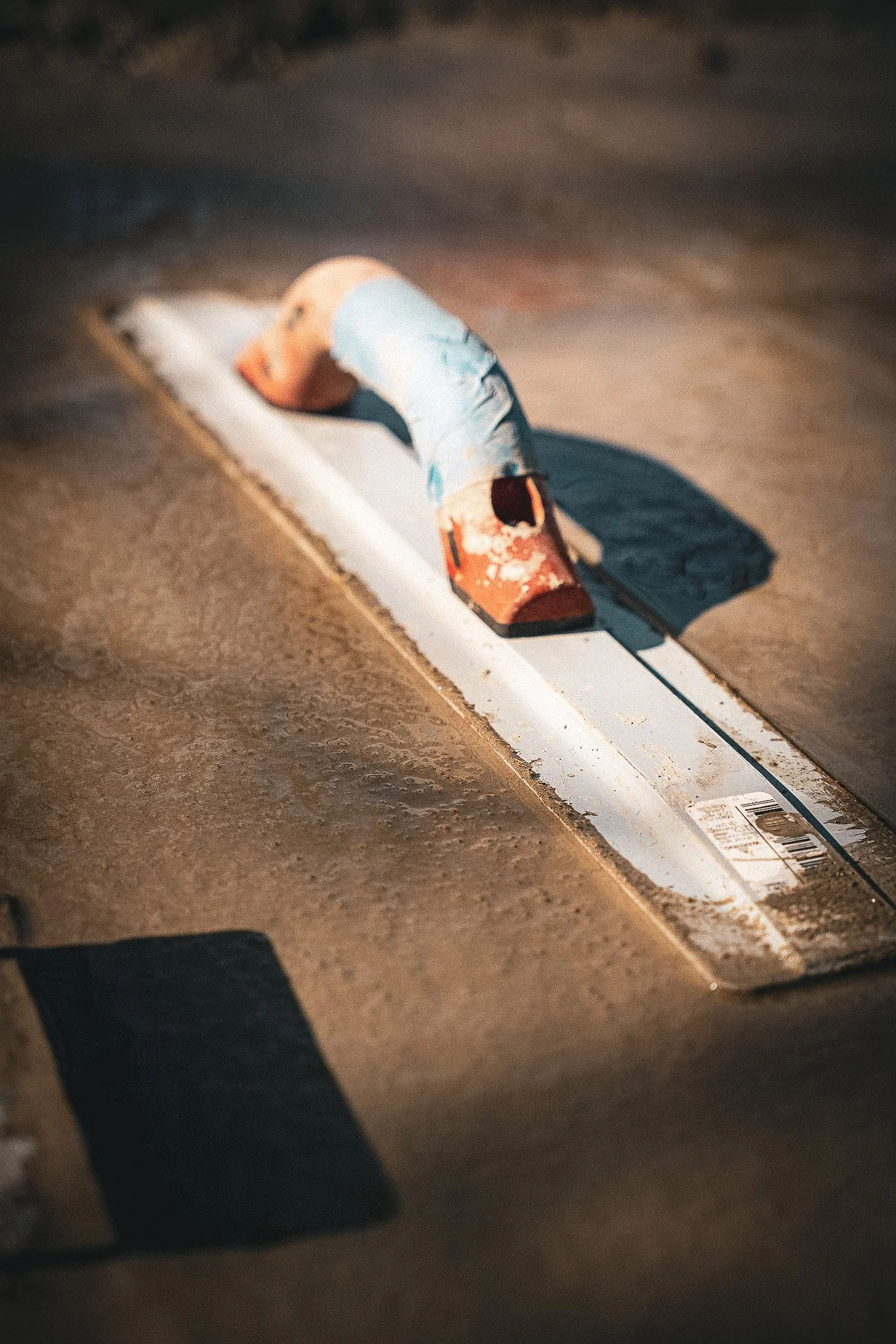 A close-up of a wooden skateboard with worn paint, placed on a dirt ground, with bright sunlight casting shadows.