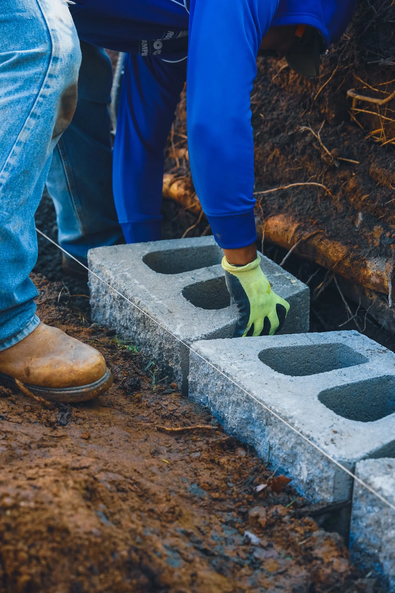 Workers laying concrete blocks for a construction project on a dirt ground.