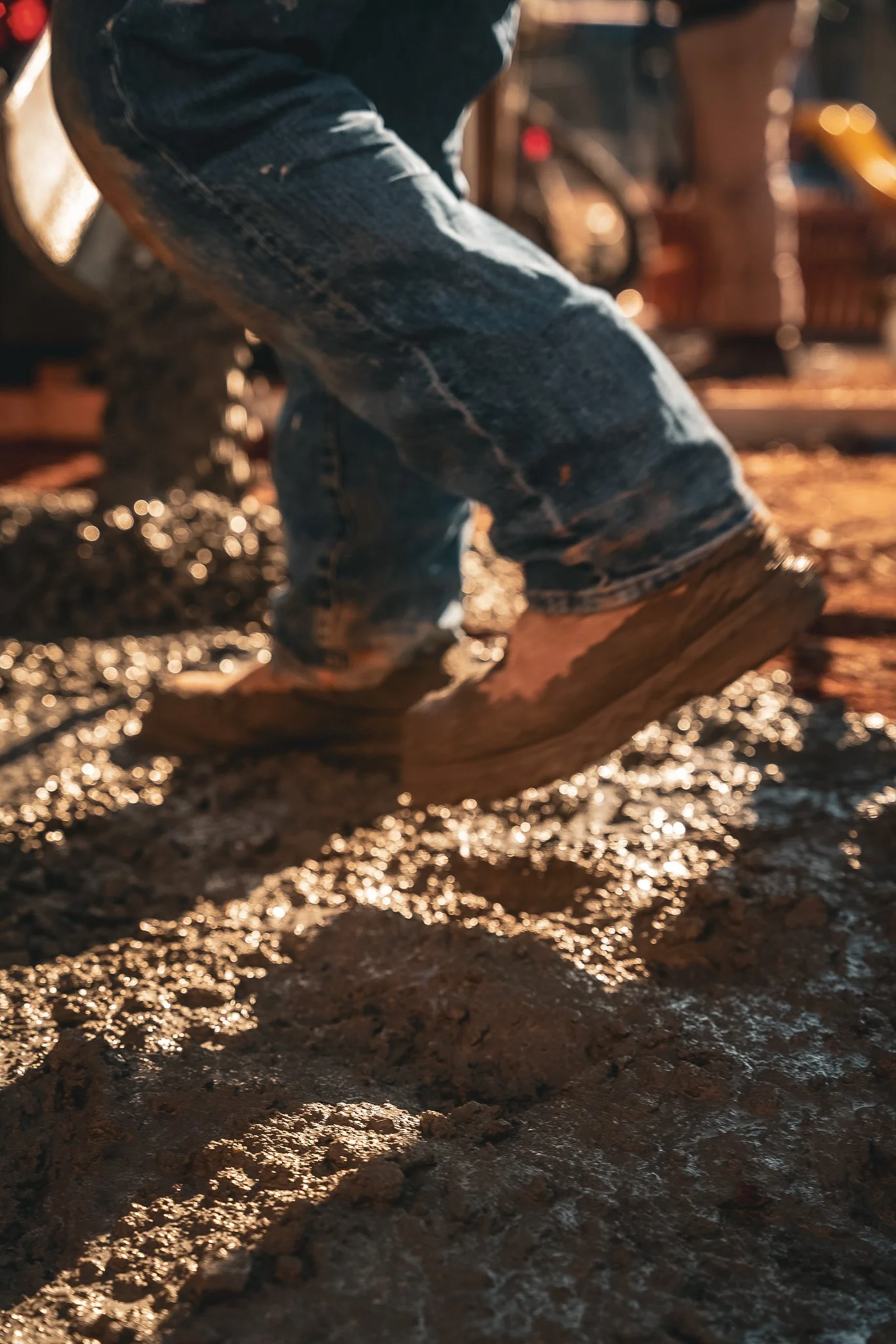 Close-up of a person's boots stepping on muddy ground, possibly outdoors in a construction or farm setting.