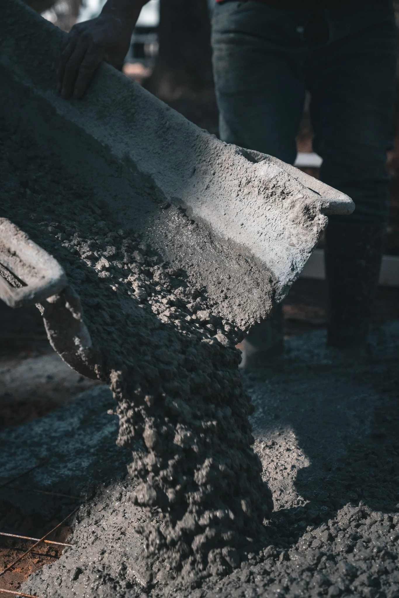 People pouring wet concrete from a wheelbarrow onto a construction site.
