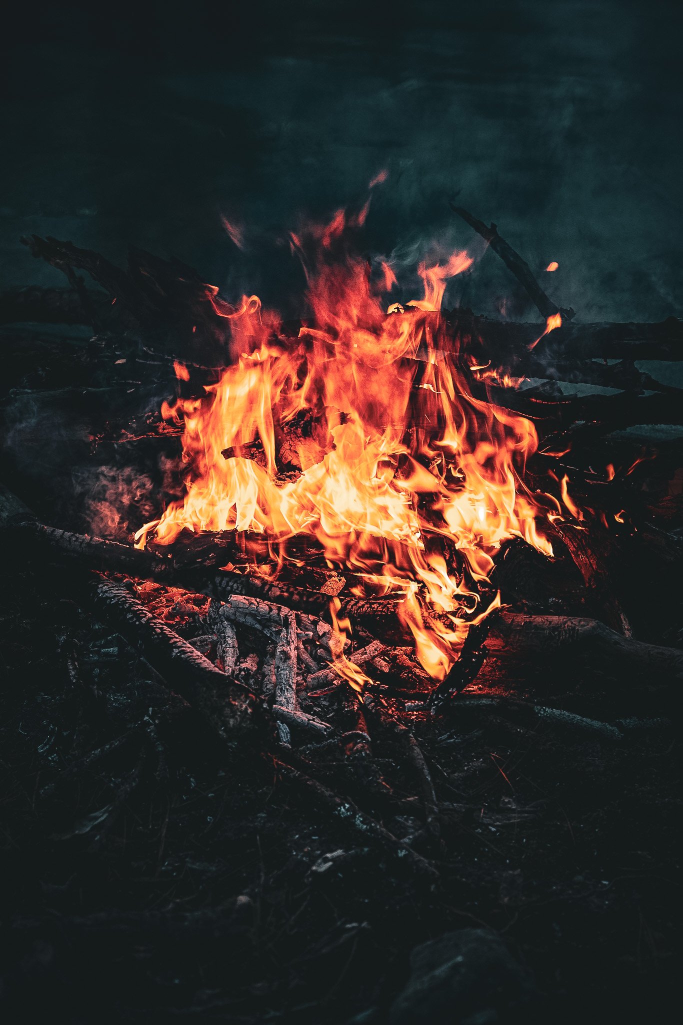 Campfire with bright orange flames burning wood and sticks against a dark background.