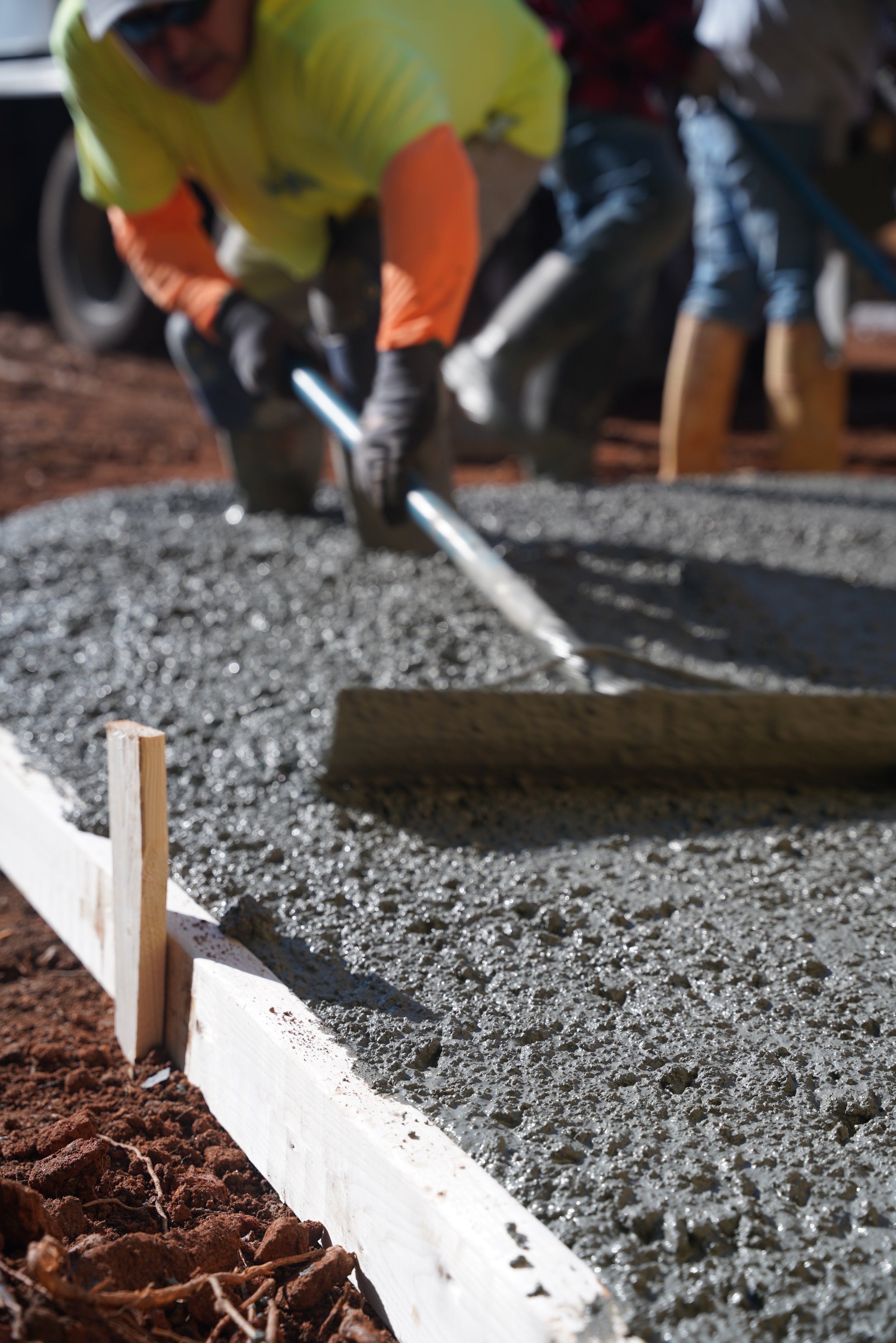 Person wearing safety gear smoothing wet concrete on a construction site.