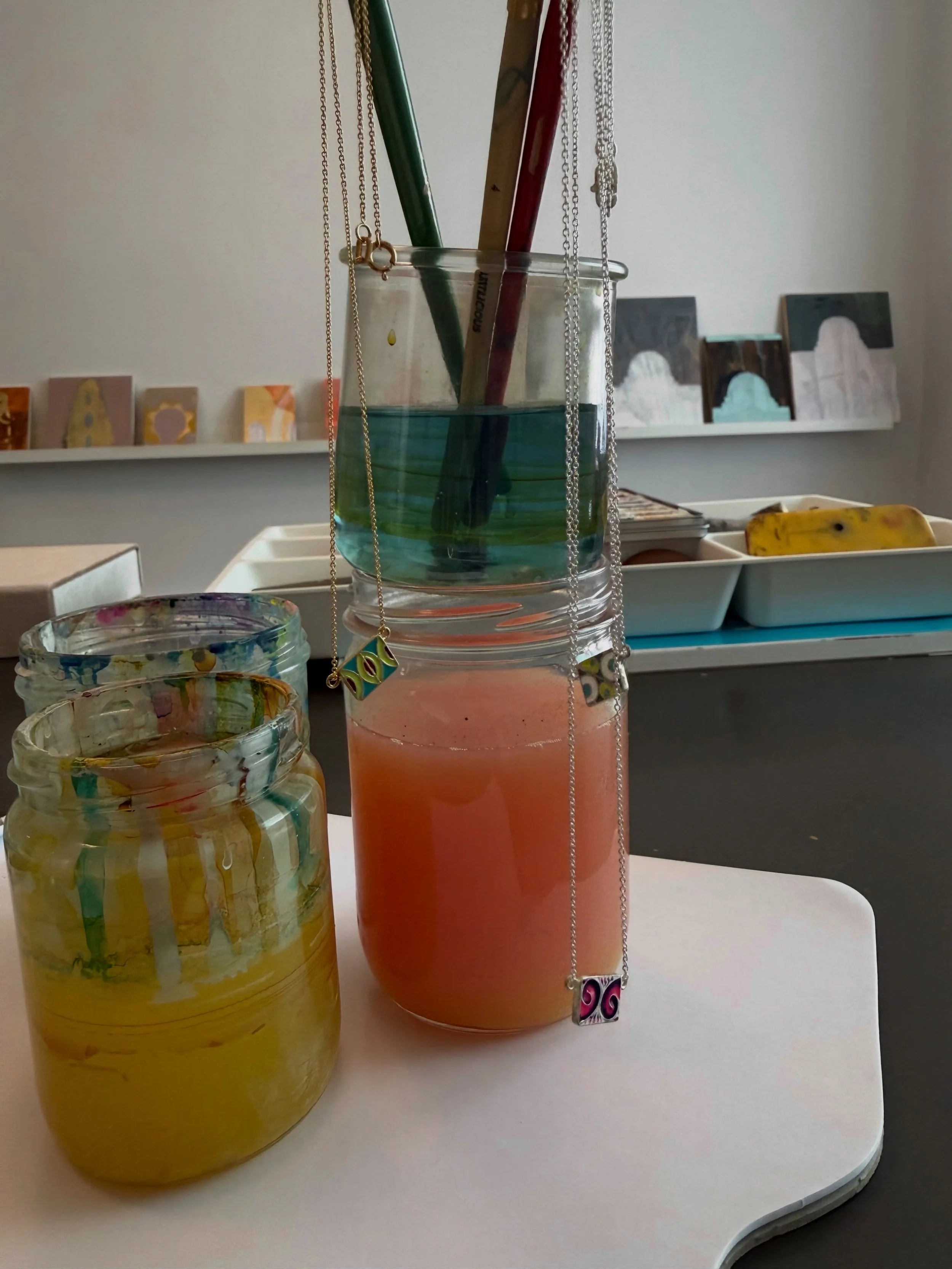 Paint jars with the prettiest colors. This past Friday I had photography of my jewelry, art and studio taken. This image incapsulates the bigger picture. If you look close you can see some of my enamel tile necklaces hanging from my paint brushes.