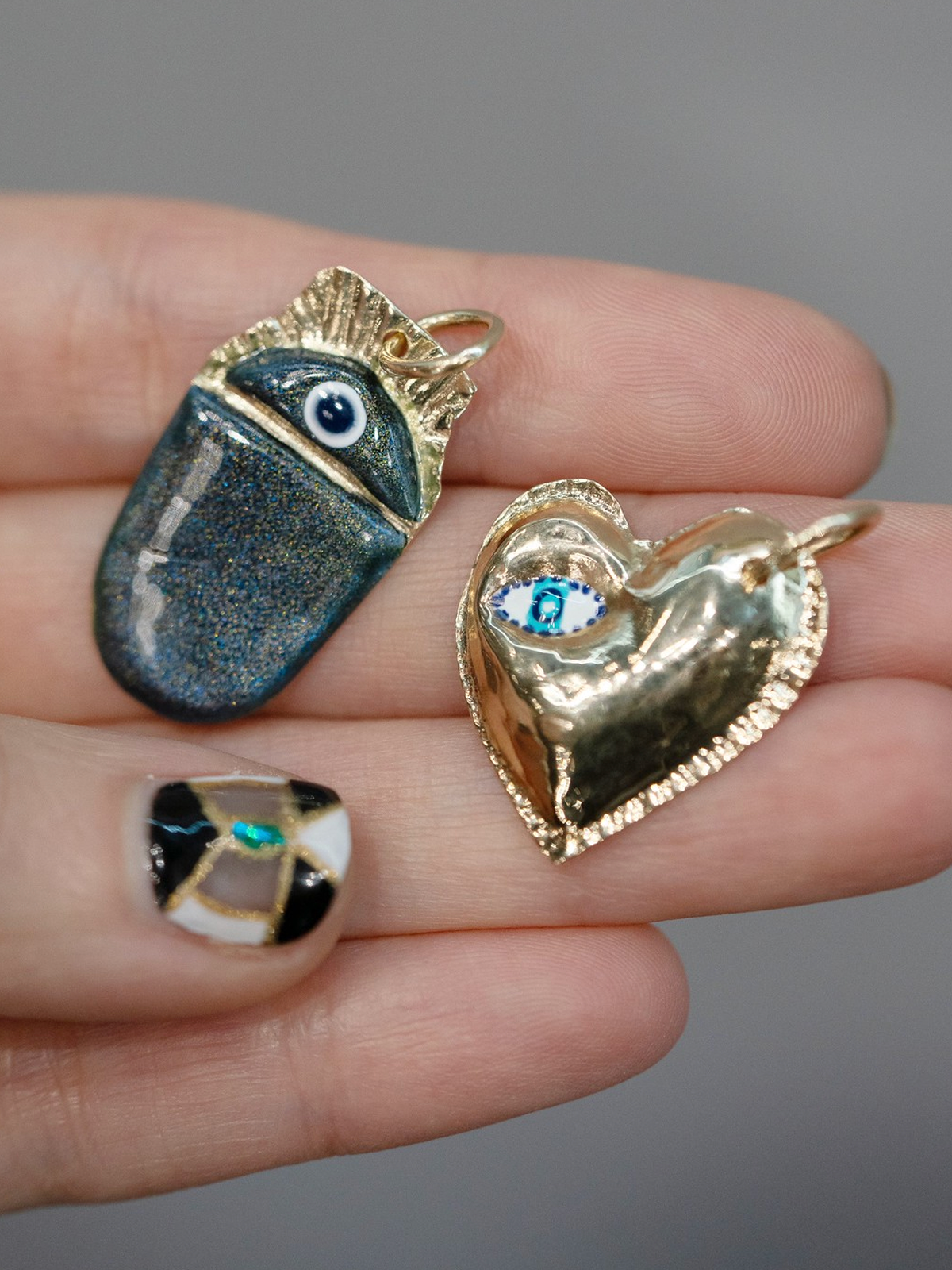 14K Gold Puffy Heart Charm with Enamel Eye on colored cord by Elaine Chong, styled in hand