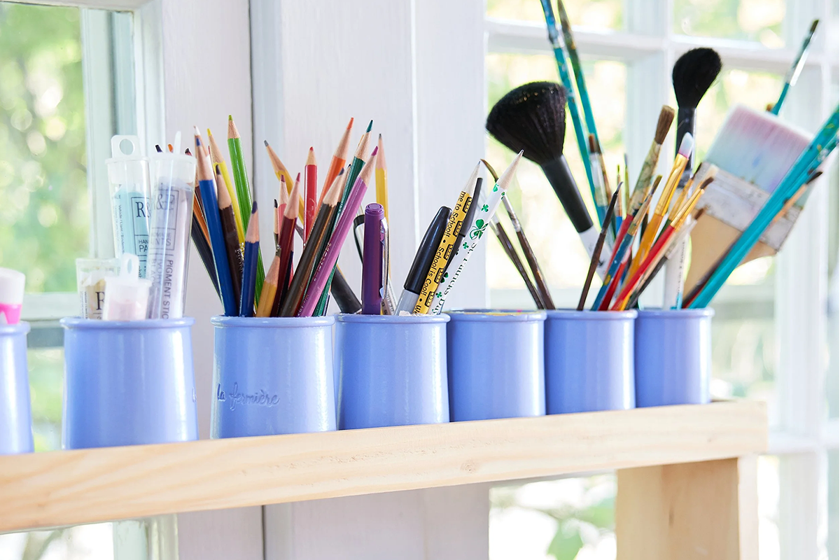 Colored pencils, brushes and art supplies on shelf next to window