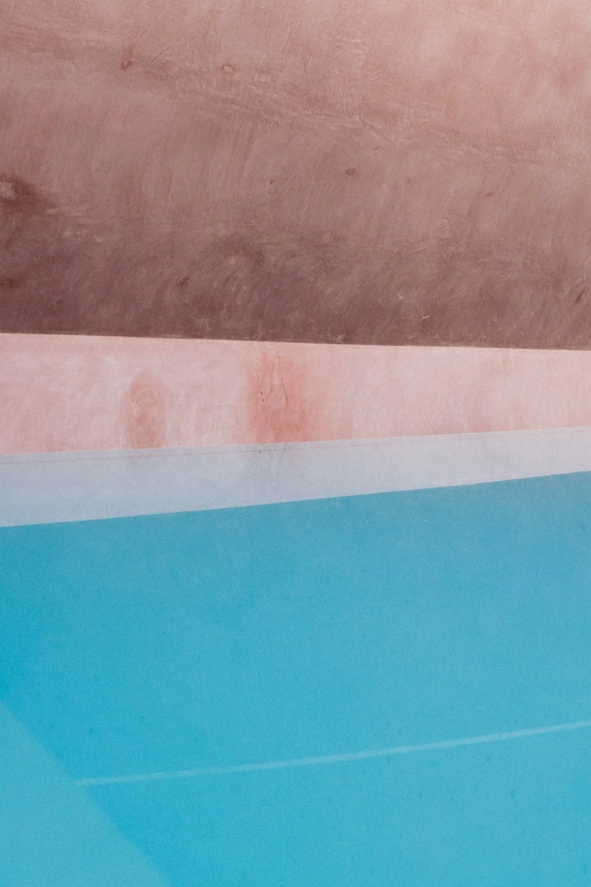 Close-up view of three layers of material, with the top layer being a rough wooden surface, the middle a smooth pinkish surface, and the bottom a smooth blue surface.