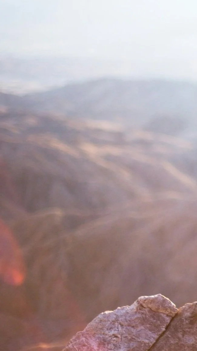 Blurred landscape with rocks in the foreground, sky in the background.
