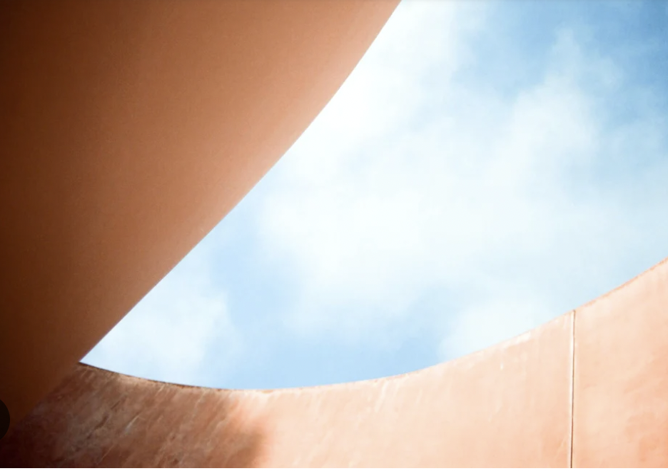 View of a round opening in a clay-colored structure looking up at a blue sky with some clouds.